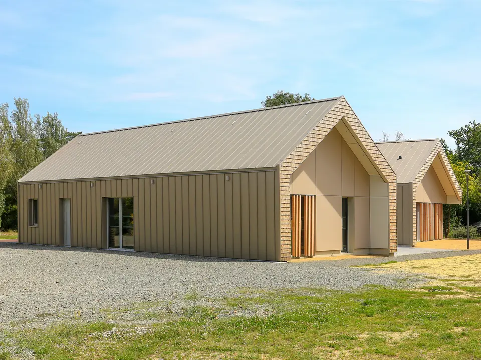 Maison de jeunesse moderne à Mûrs-Erigné, France, avec toiture PREFALZ durable et revêtement de façade en bronze. La toiture en aluminium à joint debout de PREFA impressionne par sa grande résistance aux intempéries et son aspect élégant - idéale pour les projets de construction durables et nécessitant peu d'entretien. La palette de couleurs élégante montre une intégration parfaite dans l'environnement.