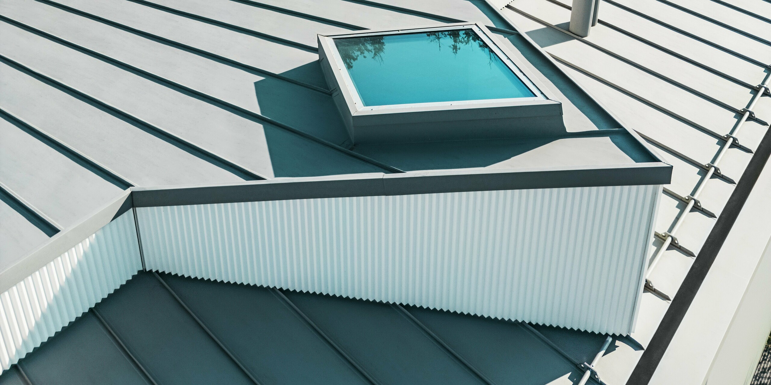 Photographie détaillée d'une toiture PREFALZ gris quartz avec puits de lumière intégré et profil dentelé vertical. La toiture à joints debout PREFA, de haute qualité, offre une résistance optimale aux intempéries et une grande précision architecturale. Associée aux lignes épurées de la façade à profil dentelé, elle crée un système de toiture moderne, durable et fonctionnel.