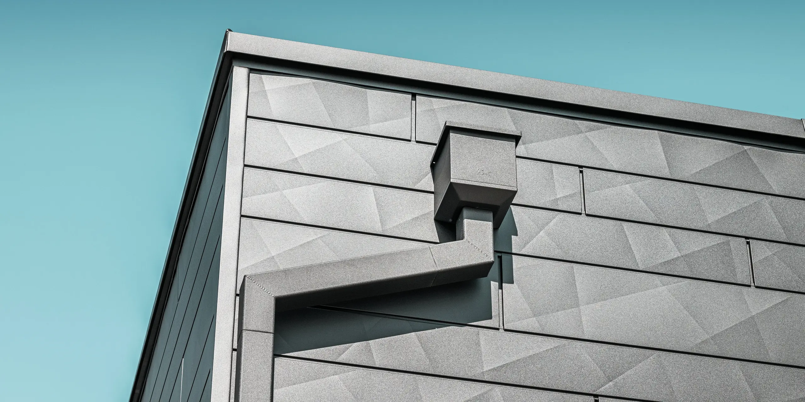 La façade de la maison individuelle rénovée de Teuschnitz est ornée de panneaux en aluminium Siding.X PREFA couleur P.10 noir, à la texture géométrique unique. Le collecteur d'eau et le tuyau carré PREFA s'intègrent élégamment au design et offrent une solution d'évacuation fonctionnelle. La finition soignée et l'intégration harmonieuse des éléments soulignent l'esthétique et la durabilité des produits en aluminium PREFA.