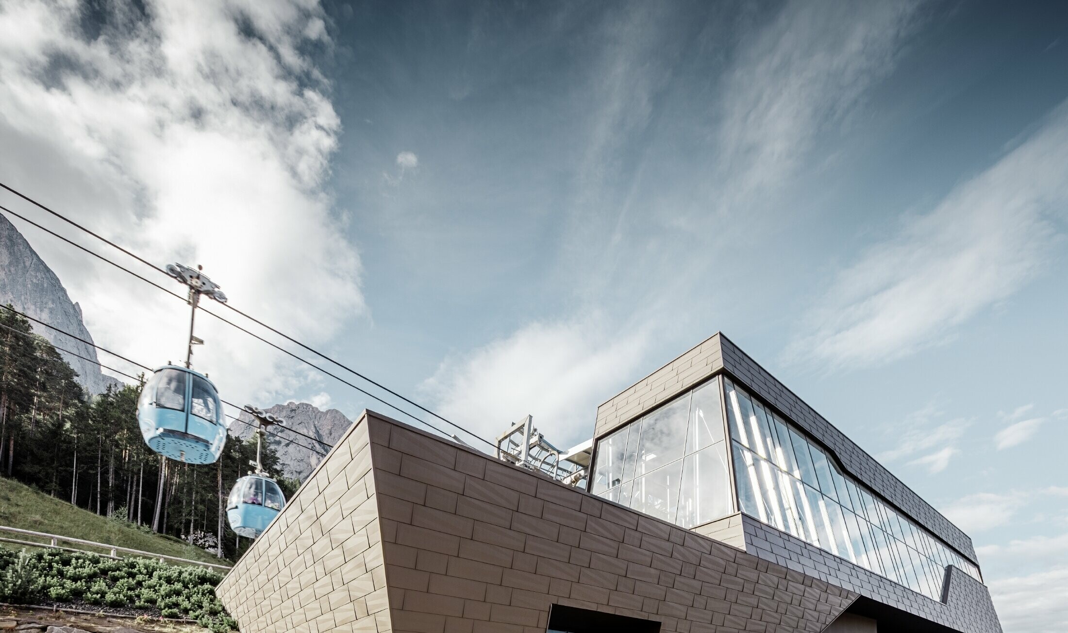 Gare de départ rénovée de la télécabine de l’Alpe di Siusi rappelant les Dolomites qui s’élèvent en toile de fond avec ses arêtes et ses surfaces irrégulières — Façade en aluminium PREFA (brun)