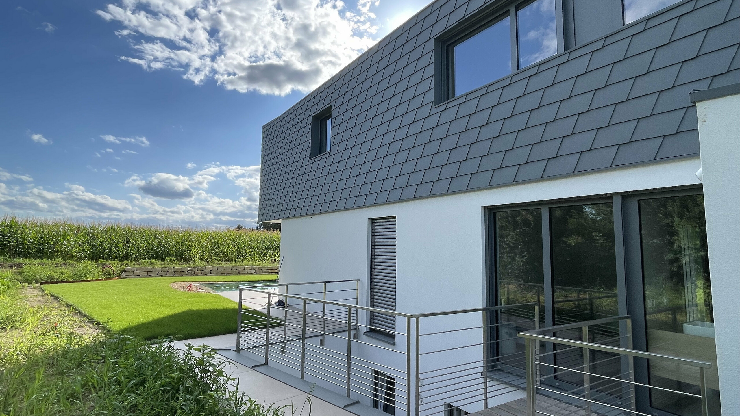Vue latérale de cette maison contemporaine dont la façade est couverte de bardeaux en aluminium PREFA dans la teinte P.10 gris souris