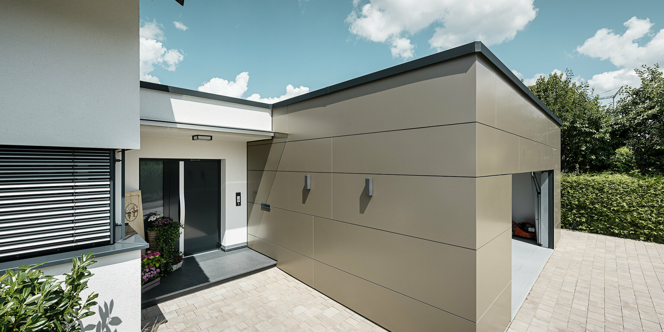 Seitliche Ansicht einer Garage mit PREFABOND Aluminium Verbundplatten in Bronze an der Fassade. Man sieht auch den Eingangsbereich des Hauses.