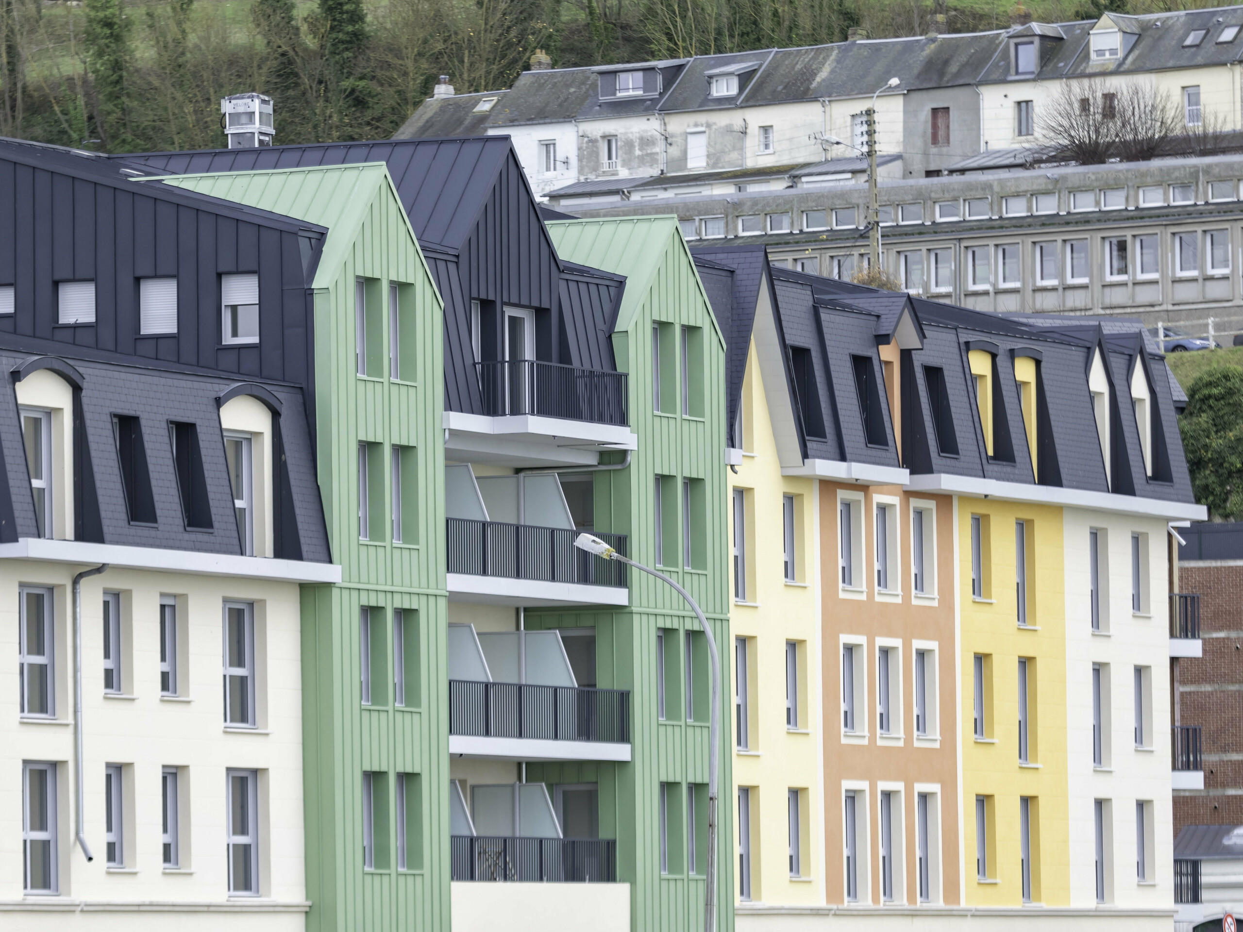 Prise de vue latérale de la résidence Le Phare à Le Tréport. On aperçoit le joint debout PREFALZ et FALZONAL dans les teintes vert olive et P.10 anthracite. S'en suivent alors des façades en crépis jaunes orangées et des toiture en ardoise.