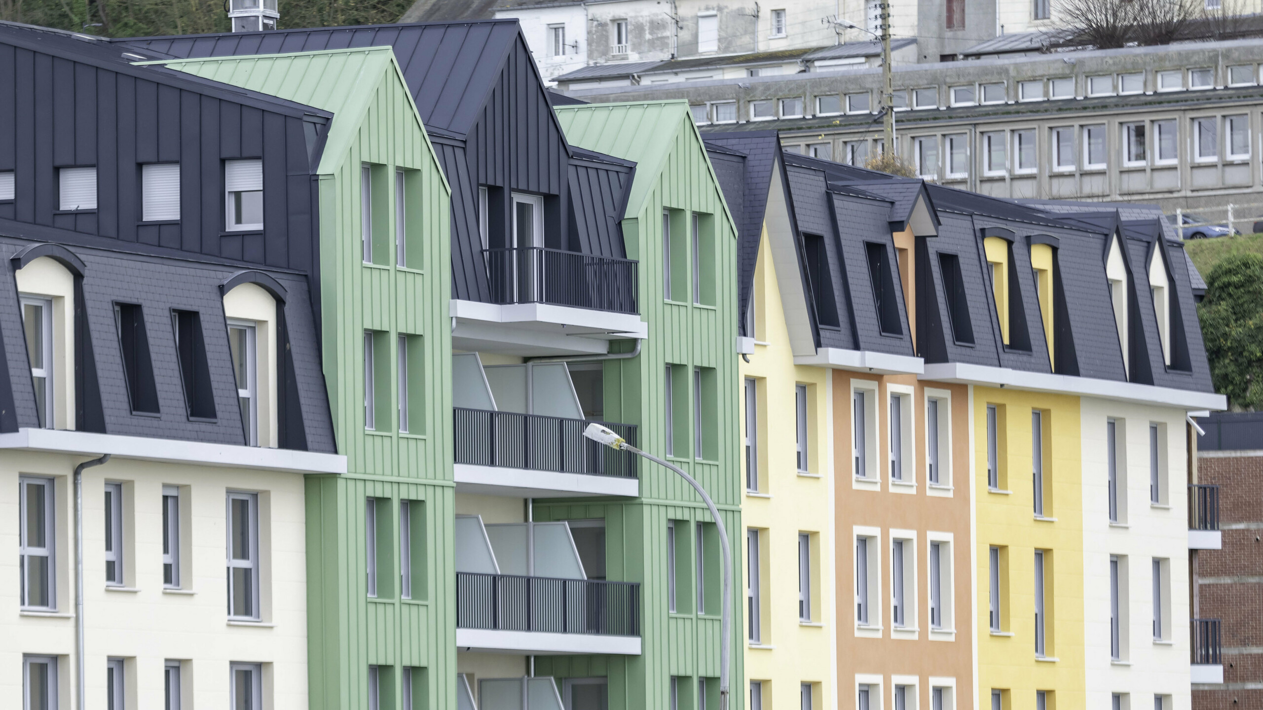 Prise de vue latérale de la résidence Le Phare à Le Tréport. On aperçoit le joint debout PREFALZ et FALZONAL dans les teintes vert olive et P.10 anthracite. S'en suivent alors des façades en crépis jaunes orangées et des toiture en ardoise.