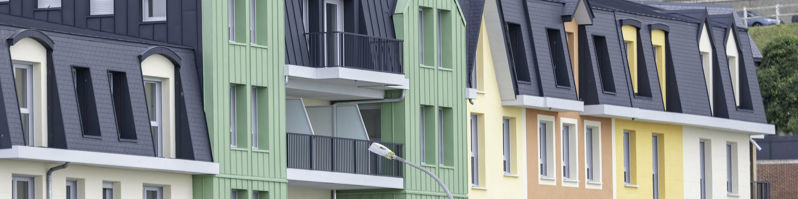 Prise de vue latérale de la résidence Le Phare à Le Tréport. On aperçoit le joint debout PREFALZ et FALZONAL dans les teintes vert olive et P.10 anthracite. S'en suivent alors des façades en crépis jaunes orangées et des toiture en ardoise.