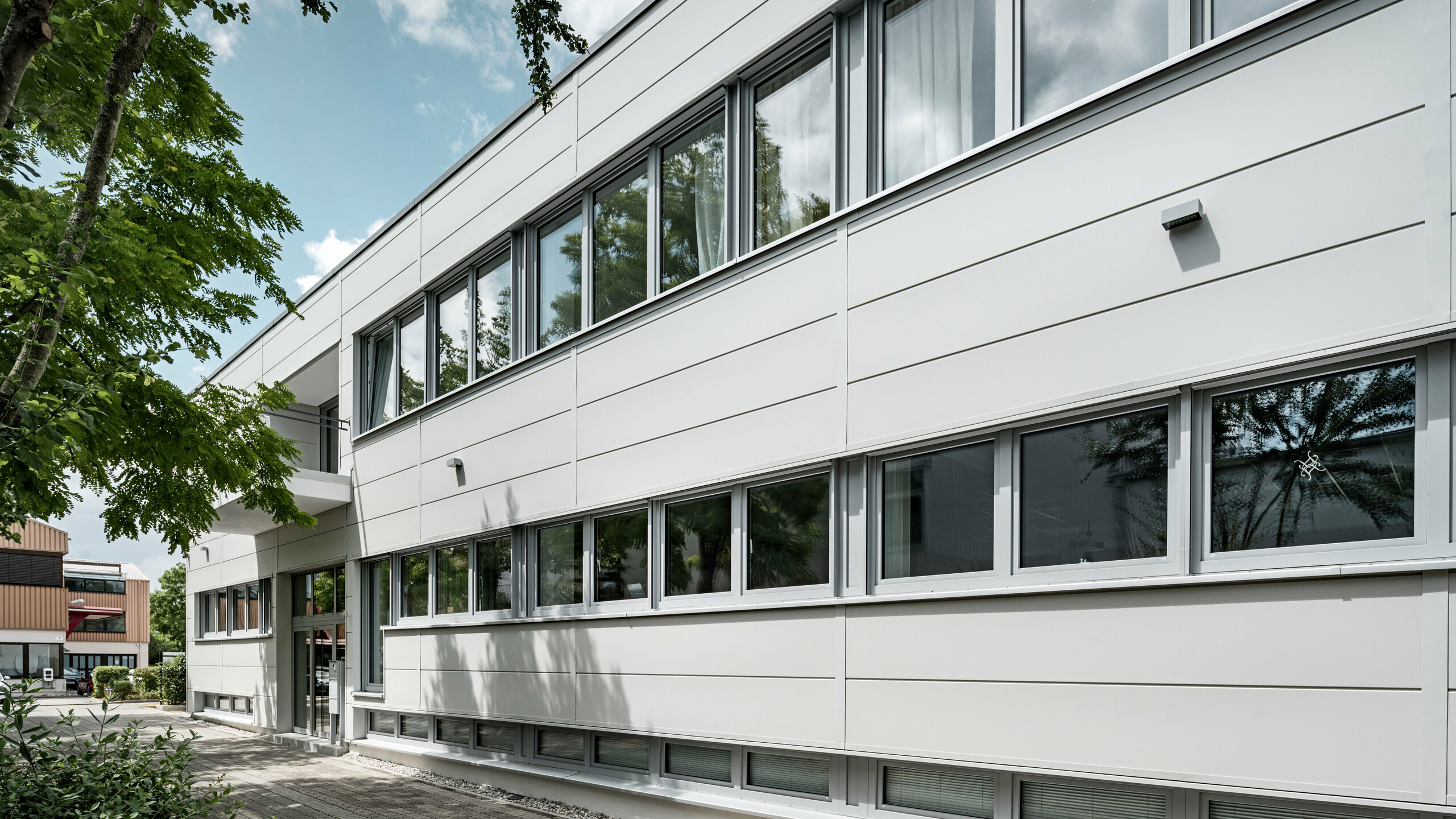 Des Sidings PREFA grand format entourent un bâtiment d'entreprise à Oberschleißheim (Allemagne). Les éléments de façade extra-larges en aluminium ont été choisis dans la couleur blanc Prefa.