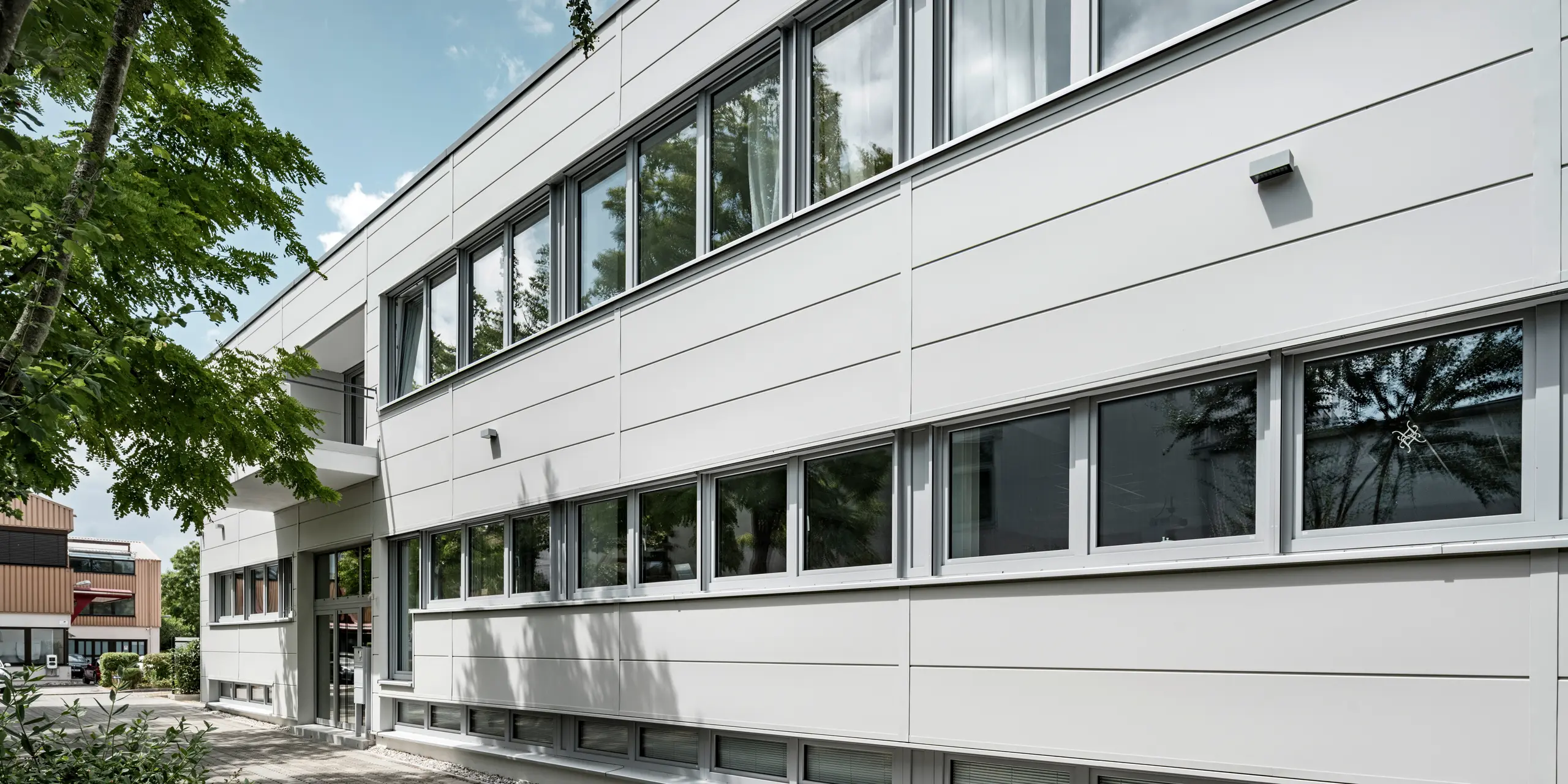 Des Sidings PREFA grand format entourent un bâtiment d'entreprise à Oberschleißheim (Allemagne). Les éléments de façade extra-larges en aluminium ont été choisis dans la couleur blanc Prefa.