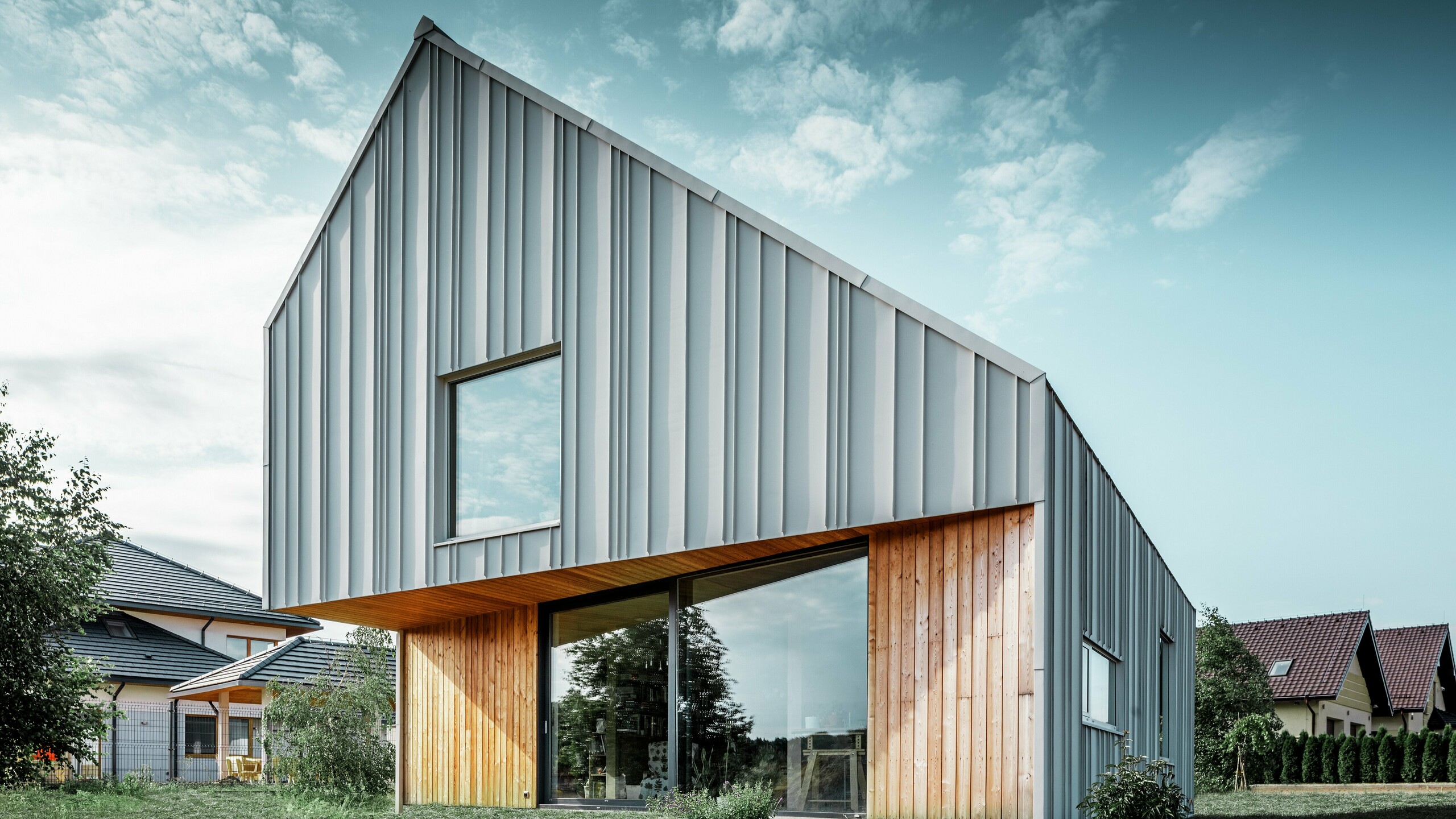 Maison individuelle moderne avec toit en pente sans avant-toit et façade en aluminium blanc de PREFA. Au rez-de-chaussée, la façade est combinée avec des panneaux de bois verticaux. 
