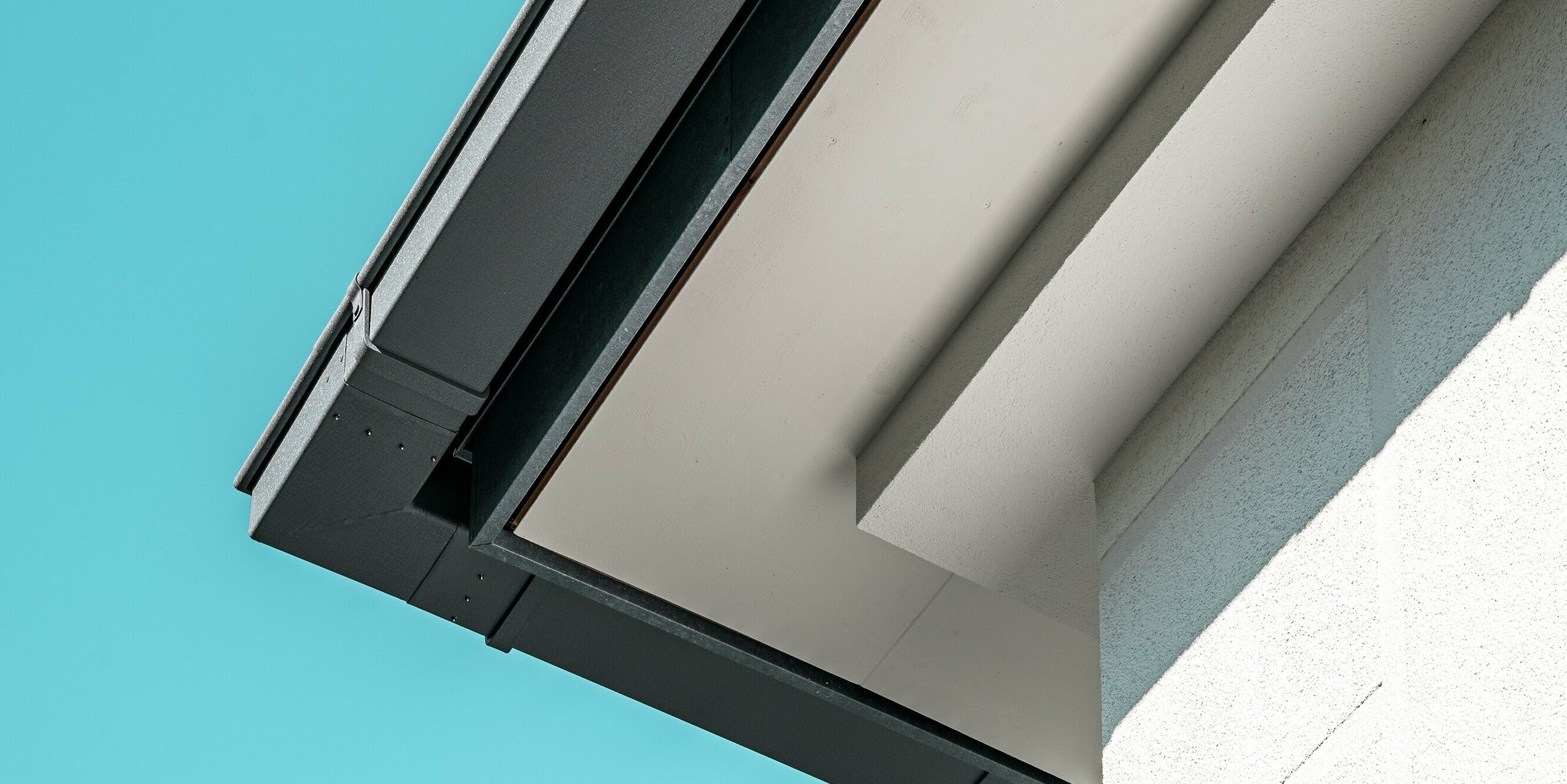 Gros plan sur la gouttière PREFA de haute qualité, coloris gris pierre P.10, qui assure une évacuation efficace des eaux. Ce système en aluminium offre des avantages à la fois esthétiques et fonctionnels. Les lignes épurées et précises de la gouttière, ainsi que son design minimaliste, s'harmonisent avec l'élégance de la maison.