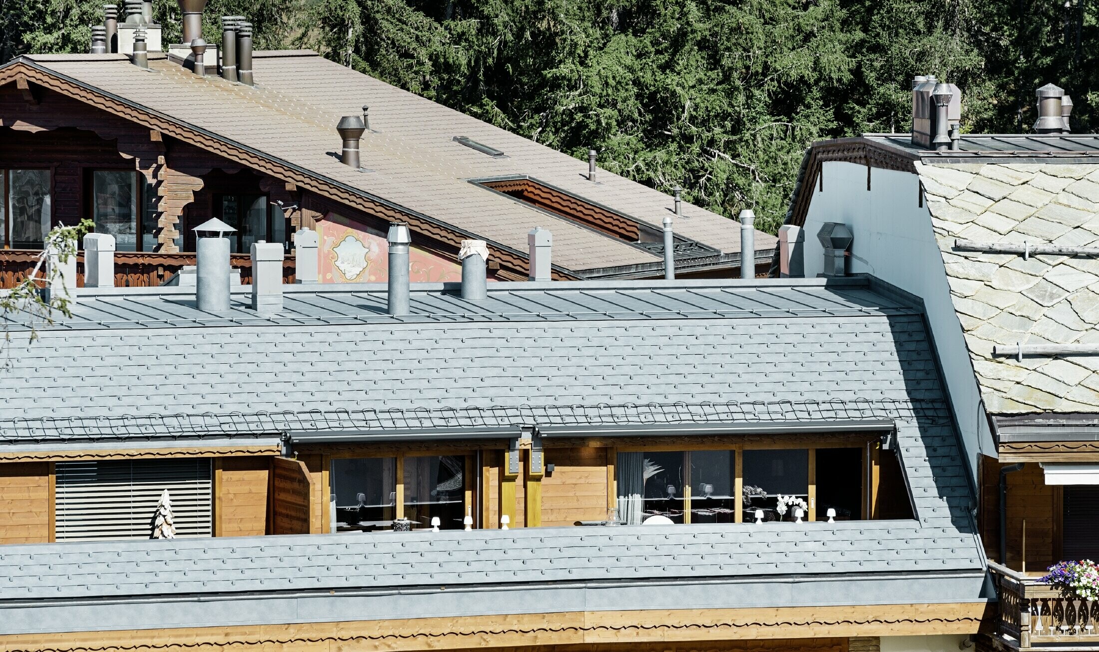 Immeuble d’habitation de Crans-Montana (Suisse) avec les Alpes en arrière-plan — Façade intégrant de nombreux éléments en bois et dont la toiture a été réalisée avec des bardeaux en aluminium PREFA de couleur gris pierre