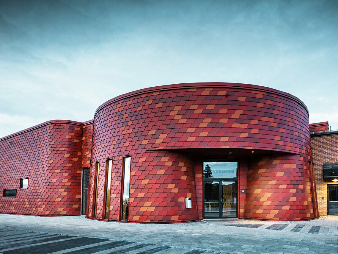 Vue de face de cette patinoire suédoise. Les bardeaux rouge oxyde s'adaptent parfaitement aux courbes du bâtiment.