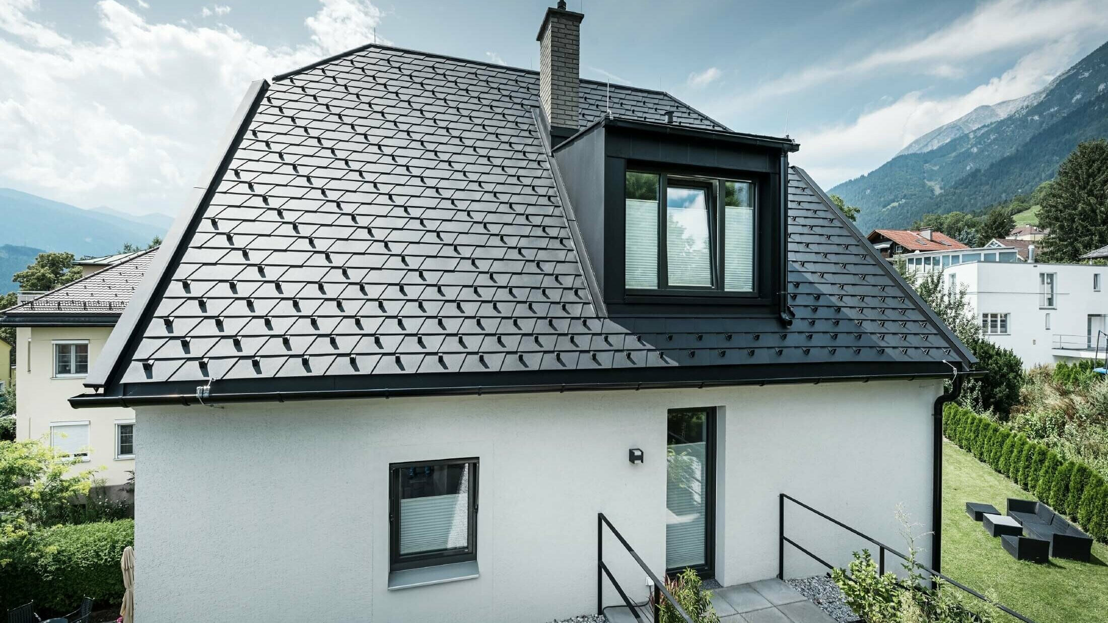 Une petite maison individuelle avec lucarne sur le toit. La toiture a été recouverte de bardeaux PREFA en P.10 noir. 