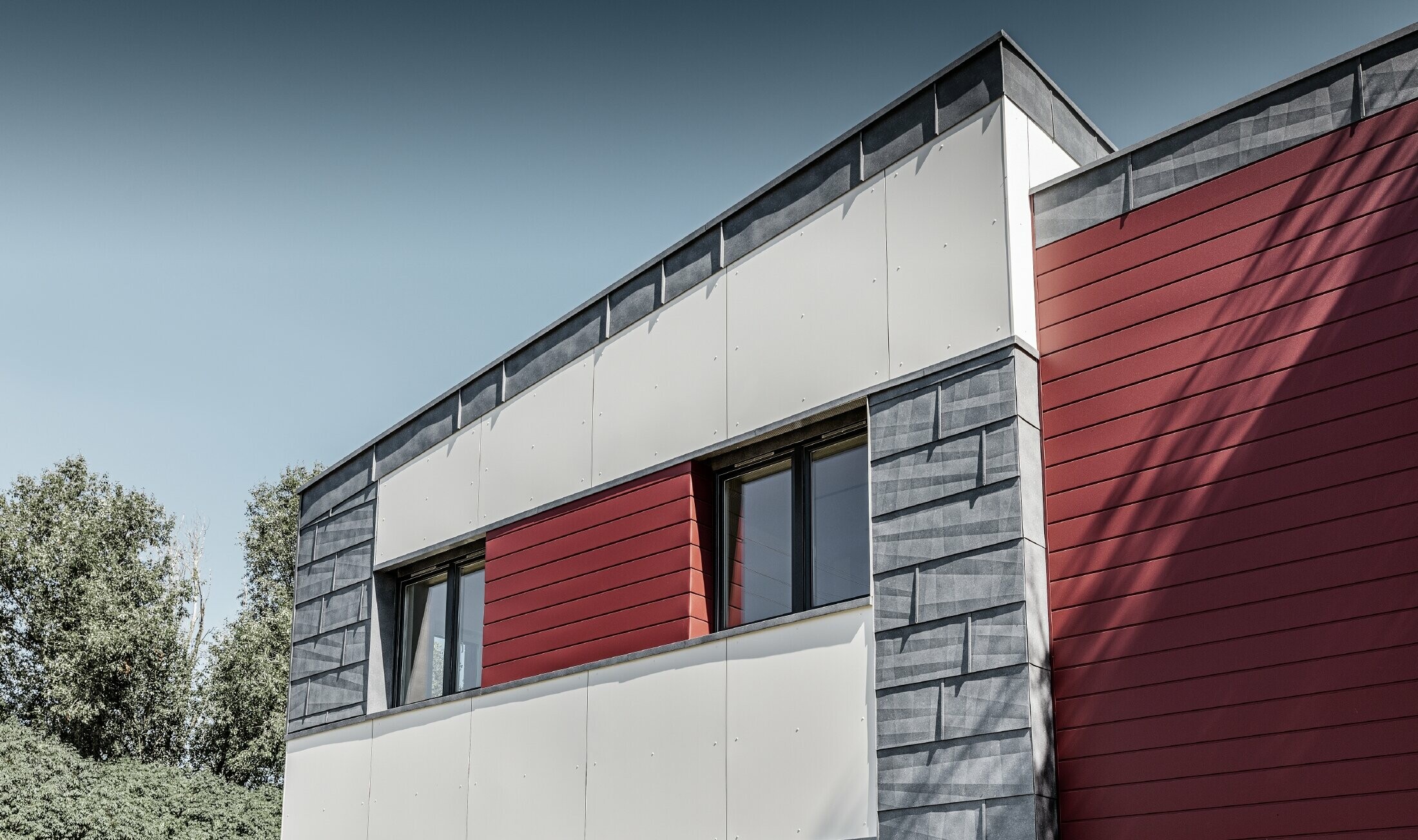 Complexe de bureaux moderne — Façade tricolore (blanc, rouge et gris pierre) réalisée à partir de produits en aluminium PREFA (sidings, panneaux de façade FX.12 et panneaux composites en aluminium)