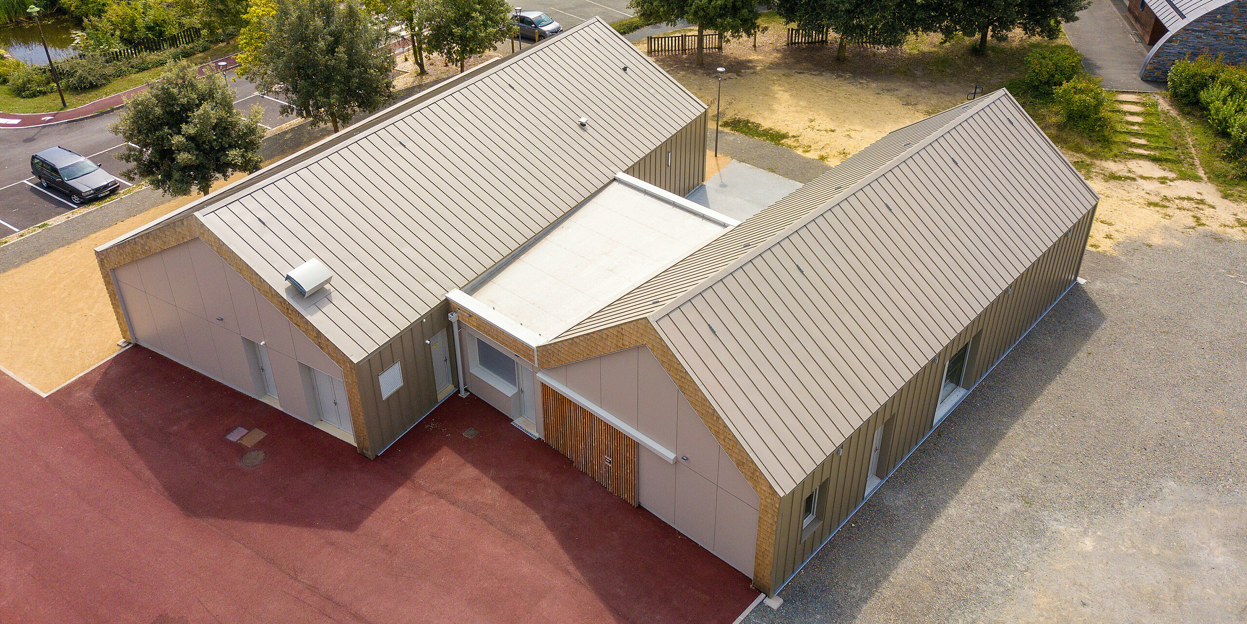 Vue aérienne de la maison des jeunes Salles Espace Bellevue à Mûrs-Erigné, France. Les deux bâtiments sont équipés d'un bardage à joint debout en PREFALZ de couleur bronze. Le revêtement en aluminium résistant aux intempéries et durable de PREFA offre une solution moderne et durable pour les projets architecturaux exigeants.