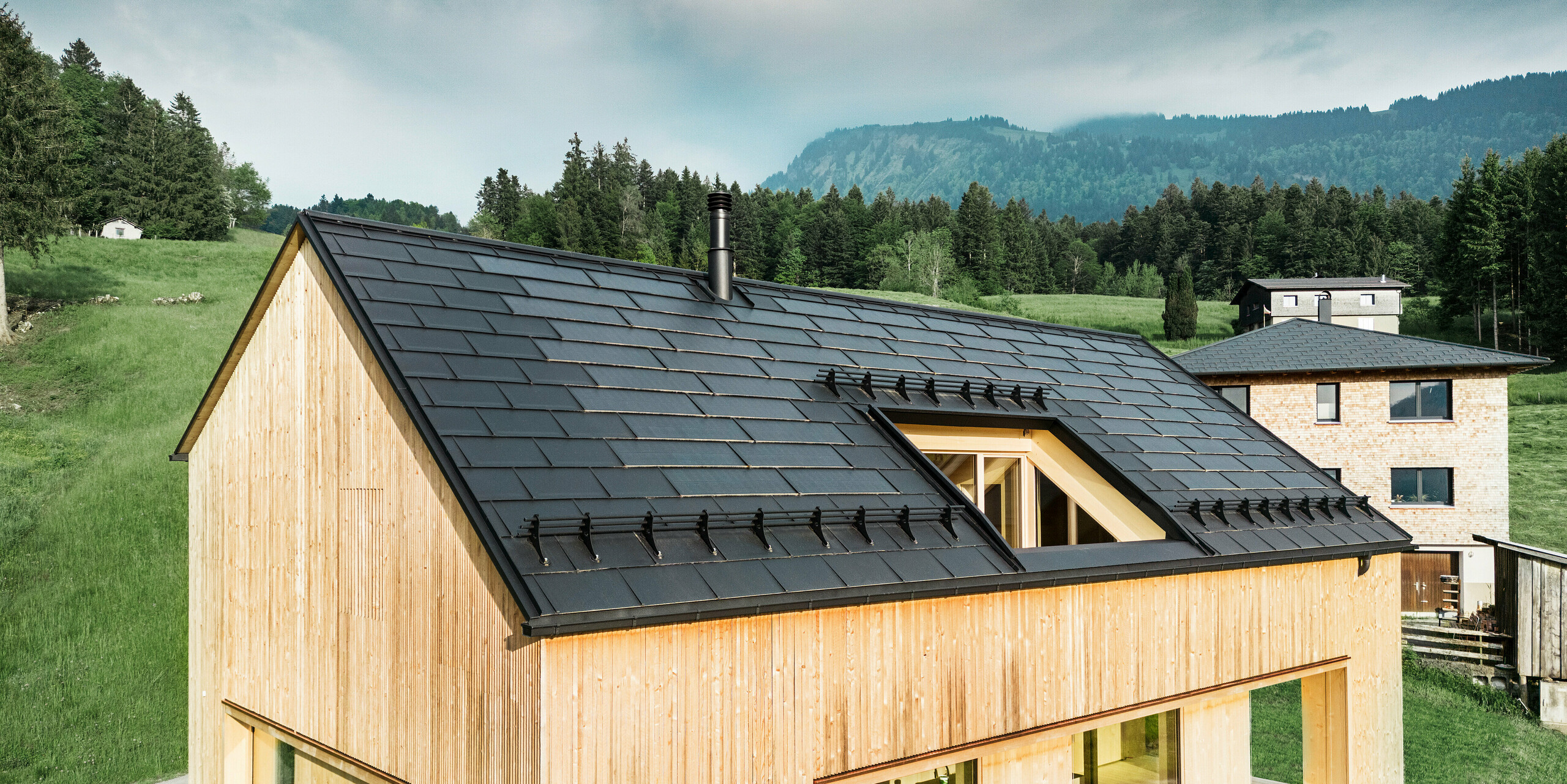 Maison individuelle dans la ville autrichienne d'Egg avec le panneau de toit solaire PREFA et le panneau de toit R.16 en noir, combinés à une façade en bois