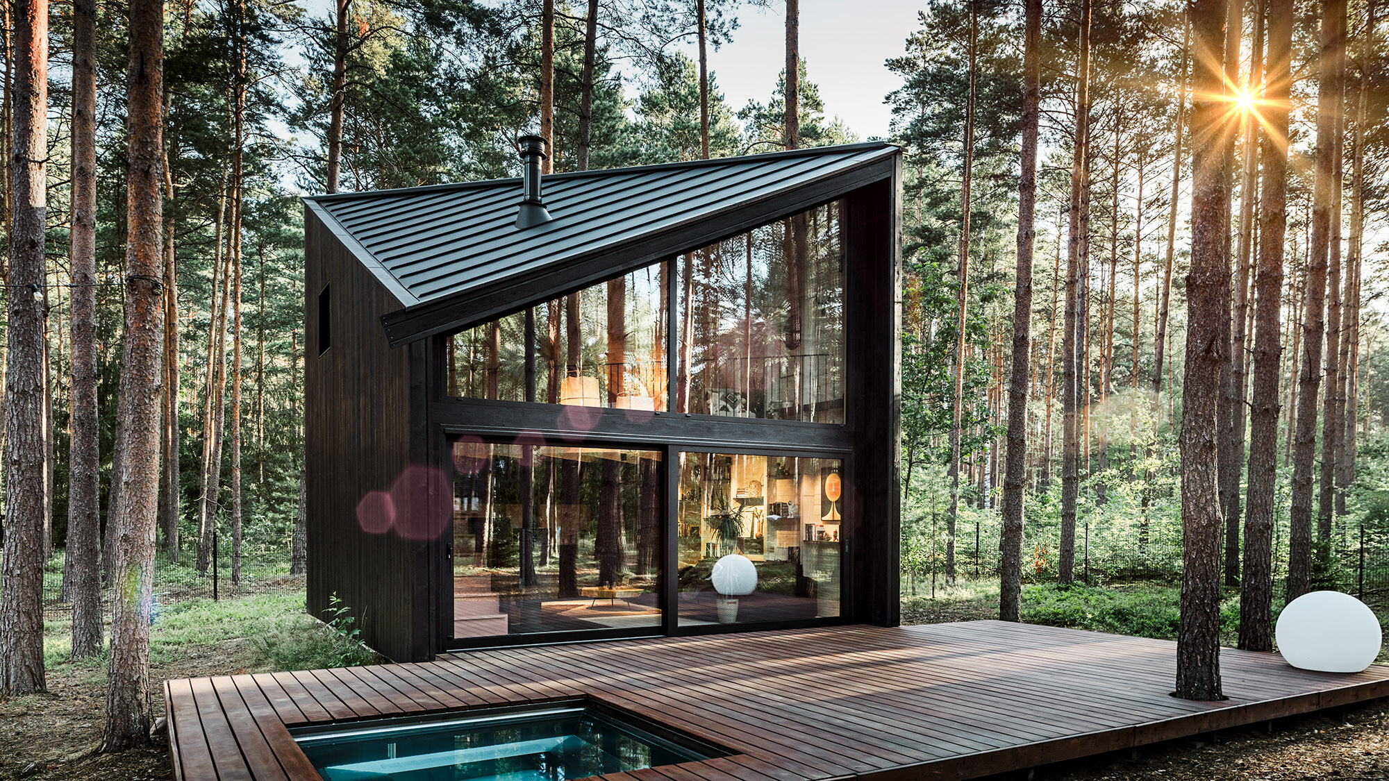 Vue latérale d'une maison de vacances avec un toit en PREFALZ en pente. La nature environnante se reflète dans la zone vitrée.