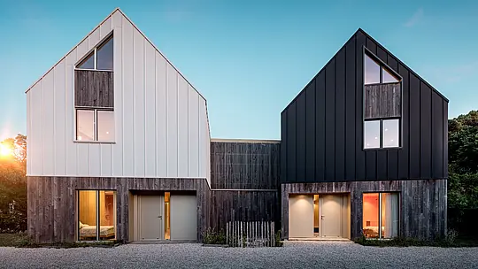 La façade du complexe résidentiel Le Rhune présente deux bâtiments décalés, à l'architecture identique, qui se distinguent par leurs contrastes de blanc et de noir. La pureté des lignes des toitures à deux pans et le revêtement continu en aluminium PREFALZ confèrent aux bâtiments une allure sculpturale et mettent en valeur la précision des joints debout. De chaleureux jeux de lumière, filtrés par les larges fenêtres, créent un contraste saisissant avec l'architecture minimaliste. L'aluminium PREFALZ, résistant aux intempéries et durable, assure la cohésion de la toiture et de la façade, formant une enveloppe de bâtiment moderne et harmonieuse, d'une grande qualité esthétique.