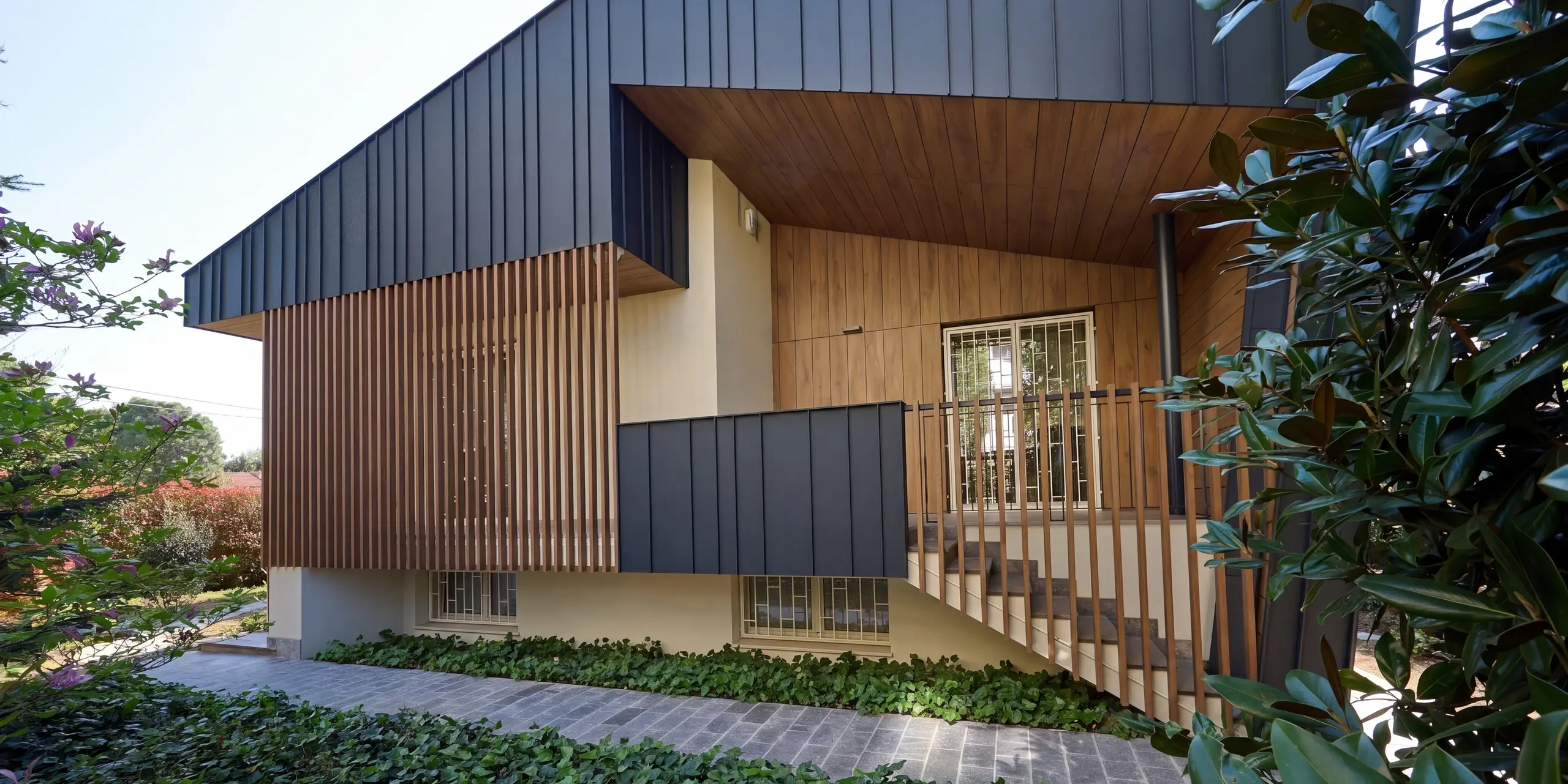 Gros plan sur la Villa Castellanza, revêtue d'une façade en aluminium PREFALZ de haute qualité, coloris anthracite P.10. Les joints debout apparents, les éléments en bois chaleureux et le généreux débord de toit créent un contraste architectural saisissant. L'aluminium PREFA confère à l'enveloppe du bâtiment une élégance indéniable, une grande résistance aux intempéries et une durabilité exceptionnelle, tout en minimisant l'entretien.