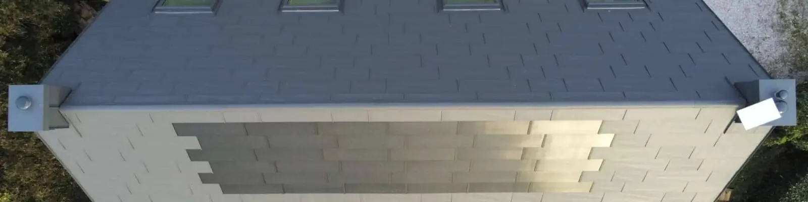 Prise de vue de haut de la toiture cette maison familiale située face à la mer, à Les Pieux. Elle a récemment été rénovée avec les produits de toiture PREFA : panneaux FX.12 et tuile solaire PREFA dans la teinte P.10 gris sombre.