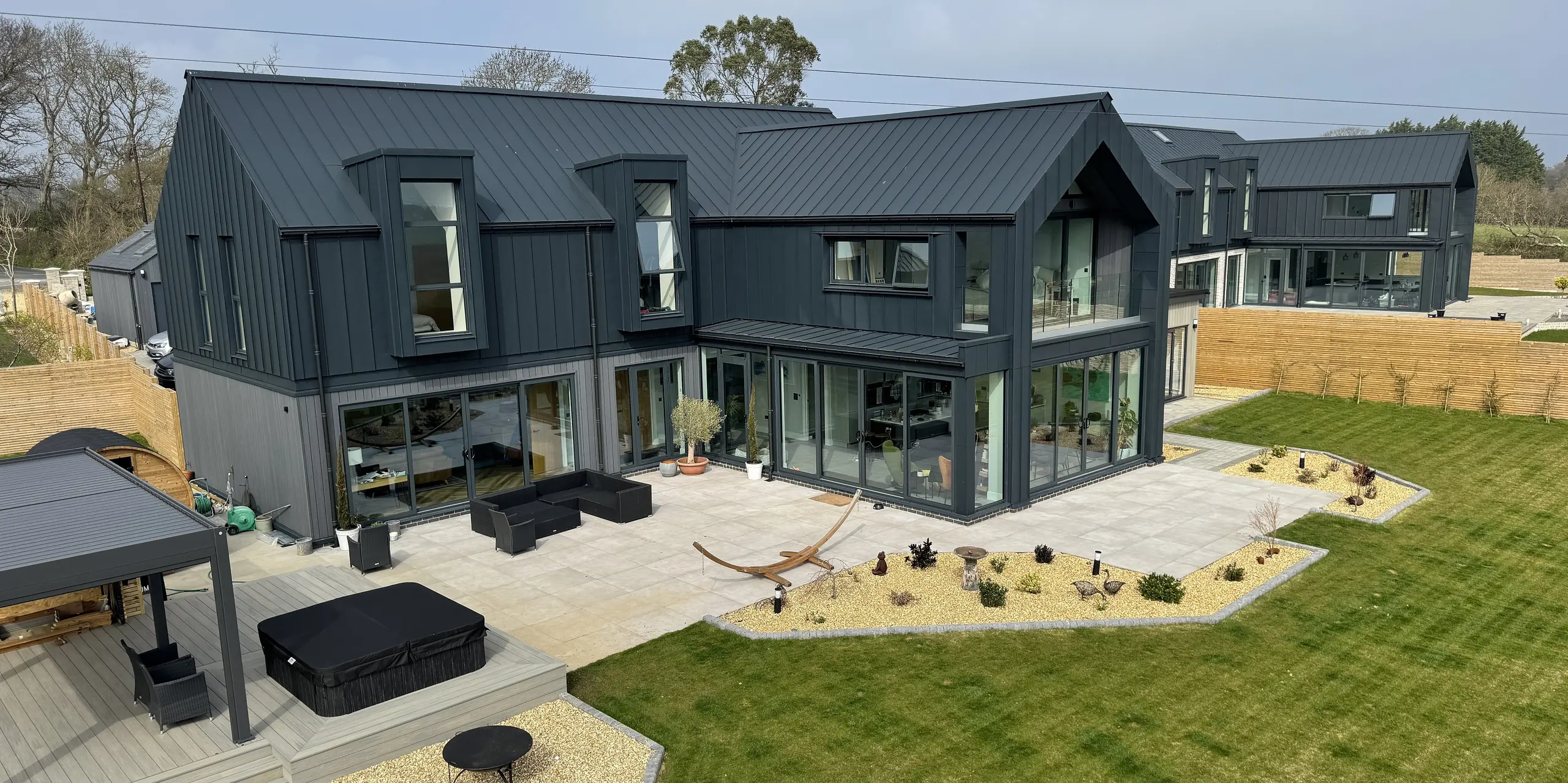 Deux maisons individuelles modernes sur l'île de Wight arborent un remarquable revêtement de toiture et de façade PREFALZ, couleur P.10 gris sombre. Leurs lignes épurées et leurs vastes façades vitrées baignent les pièces de lumière. Résistantes à la corrosion, durables et faciles d'entretien, les surfaces en aluminium sont idéales pour un environnement côtier. Au rez-de-chaussée, différents matériaux apportent des touches subtiles et confèrent à l'ensemble une personnalité unique. L'alliance d'une architecture contemporaine et des produits PREFA haut de gamme fait de ce projet un véritable chef-d'œuvre.