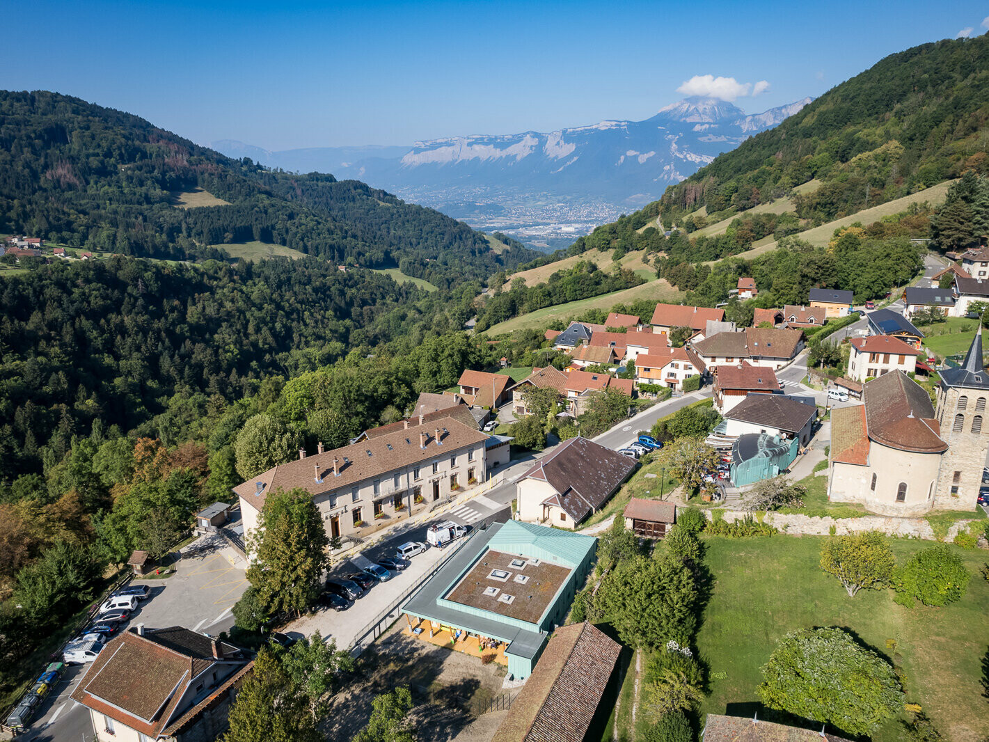 Vue de drone de la nouvelle crèche des Adrets dont la couverture en aluminium dans la teinte P.10 vert-de-gris rappelle le bâtiment historique en cuivre à quelques pas dans la commune.