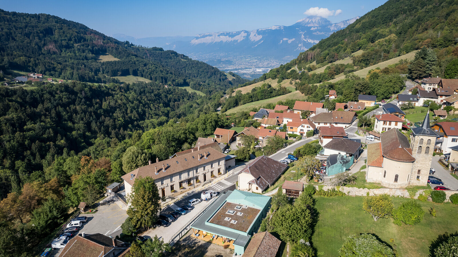 Vue de drone de la nouvelle crèche des Adrets dont la couverture en aluminium dans la teinte P.10 vert-de-gris rappelle le bâtiment historique en cuivre à quelques pas dans la commune.