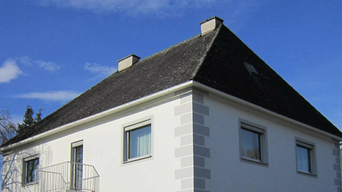 Maison avec toit à croupes avant la rénovation de toiture à l’aide de Prefalz et de tuiles PREFA, en Autriche