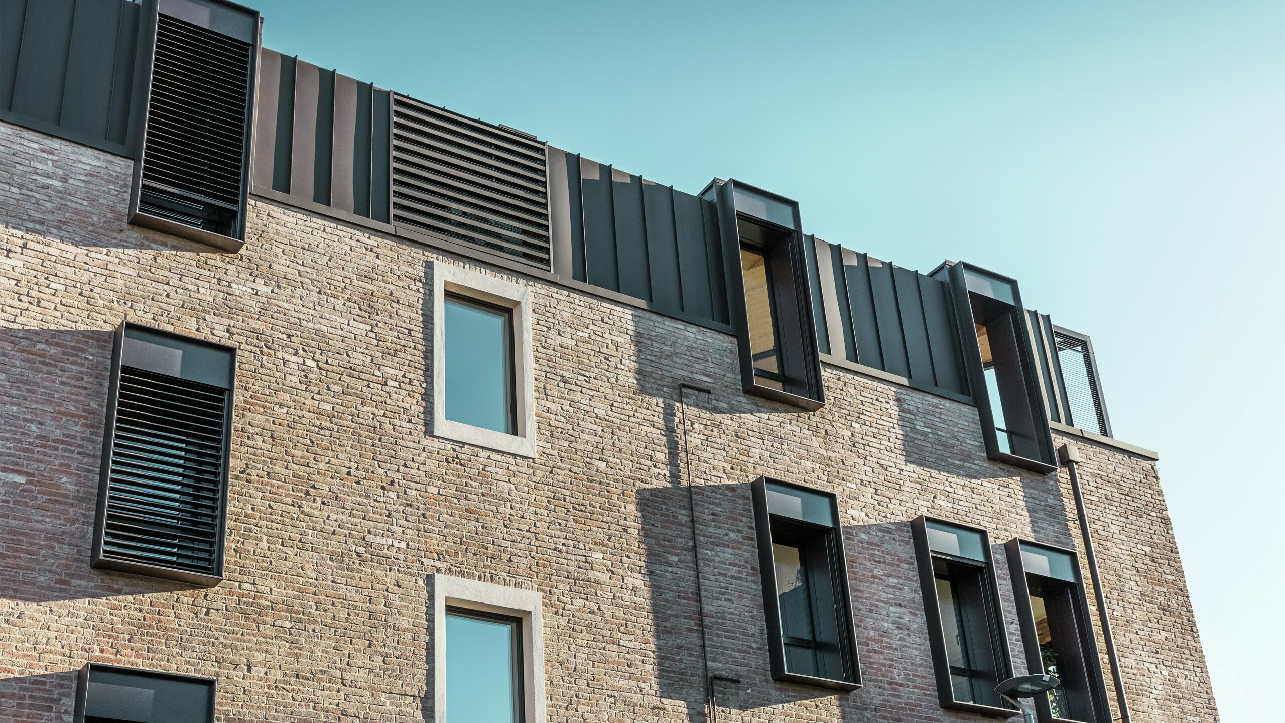 Vue détaillée d'une maison en briques rénovée en Italie avec une toiture en aluminium PREFALZ en P.10 brun noisette et des lucarnes modernes – une combinaison réussie entre la construction traditionnelle en briques et l'architecture contemporaine.