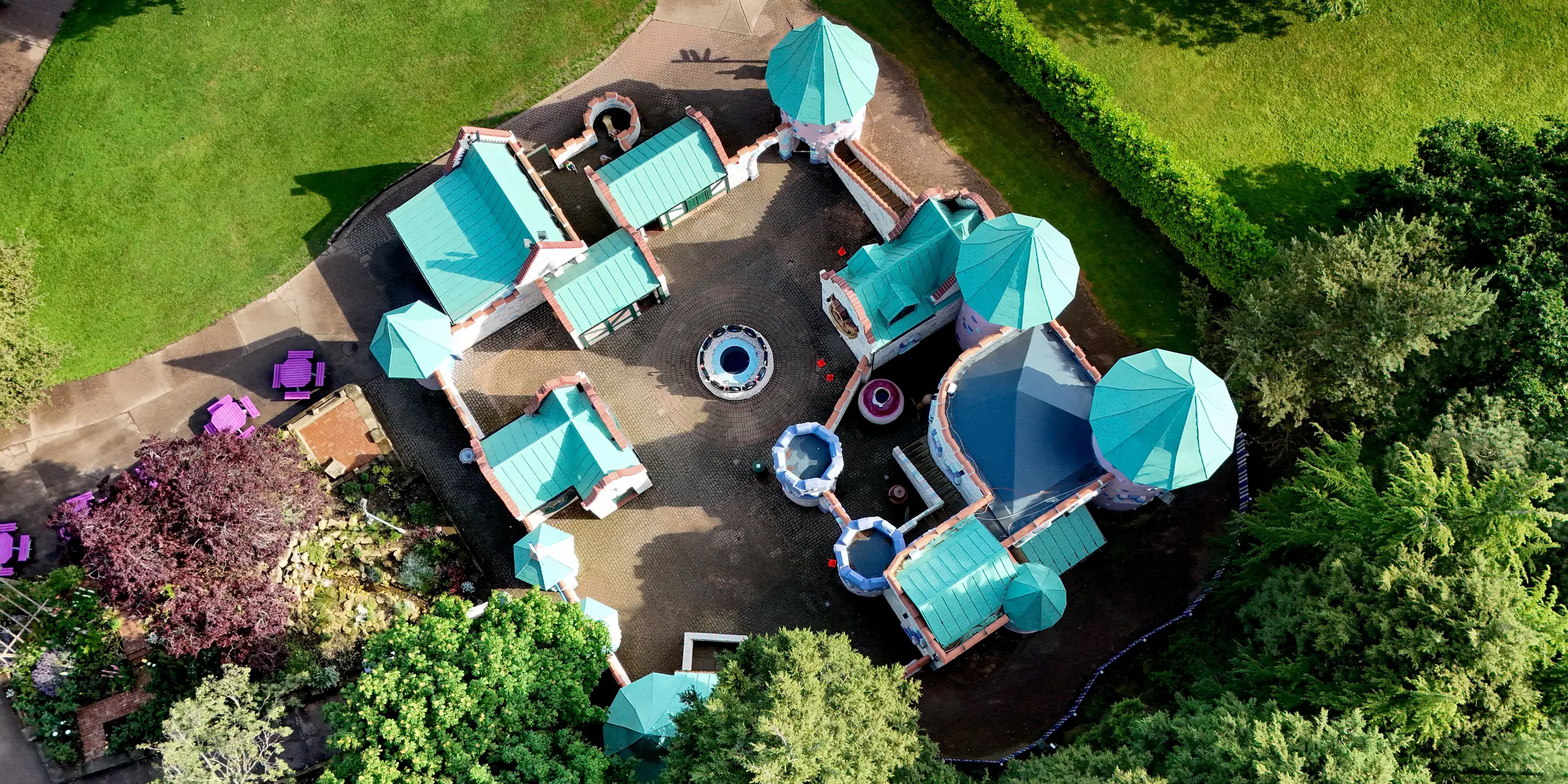 Images aériennes du complexe féerique du château de Sundown Adventureland dans le Nottinghamshire, révélant plusieurs tours originales, des plans complexes et d'impressionnants toits coniques. Les toitures en aluminium PREFALZ, couleur P.10 vert de gris, attirent immédiatement le regard et s'harmonisent avec les façades aux teintes pastel et le parc verdoyant. La netteté des joints debout souligne la géométrie complexe et témoigne de la grande malléabilité du matériau. Par ailleurs, les toitures PREFA impressionnent par leur durabilité, leur résistance à la corrosion et leur protection fiable face aux intempéries.