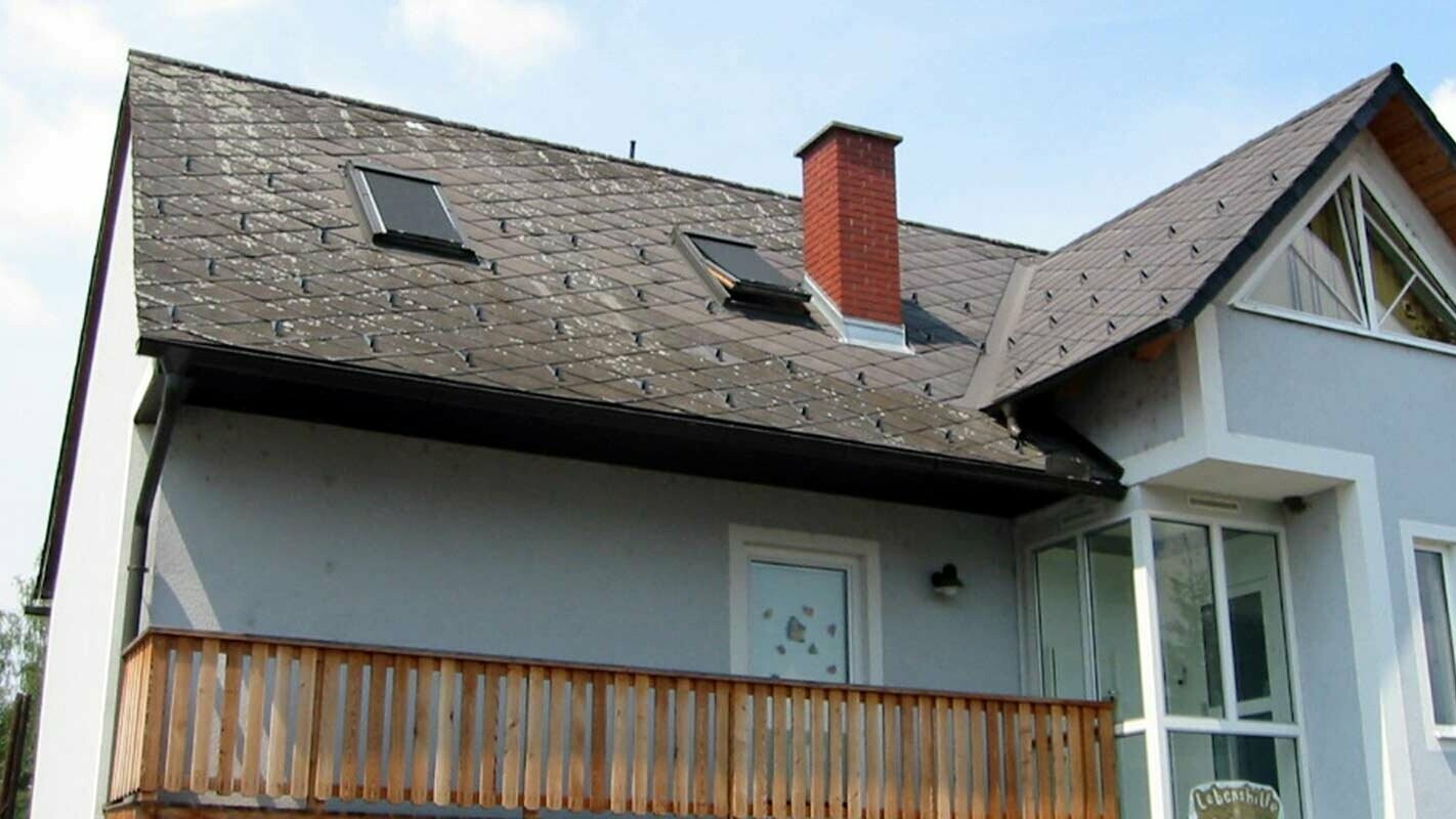 Maison individuelle avec toit à deux pans, façade bleue, cheminée en brique, toit ancien prêt à être rénové