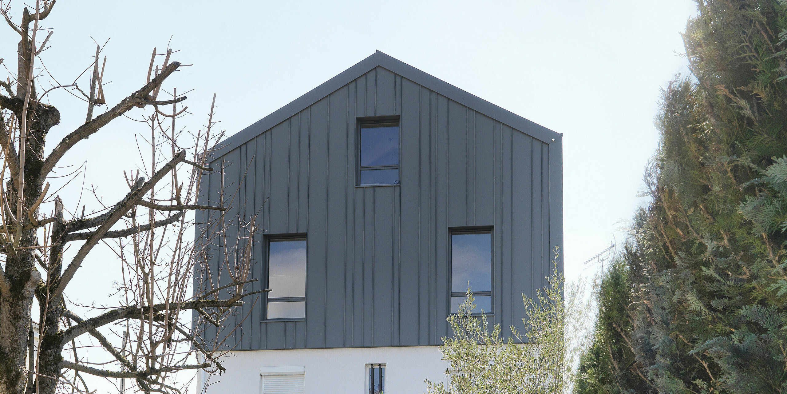 Vue depuis le jardin d'une maison familiale à Houilles (France). Pour le bâtiment, les Siding PREFA en P.10 blanc pur ont été combinés en façade et PREFALZ en P.10 gris souris en toiture et façade.