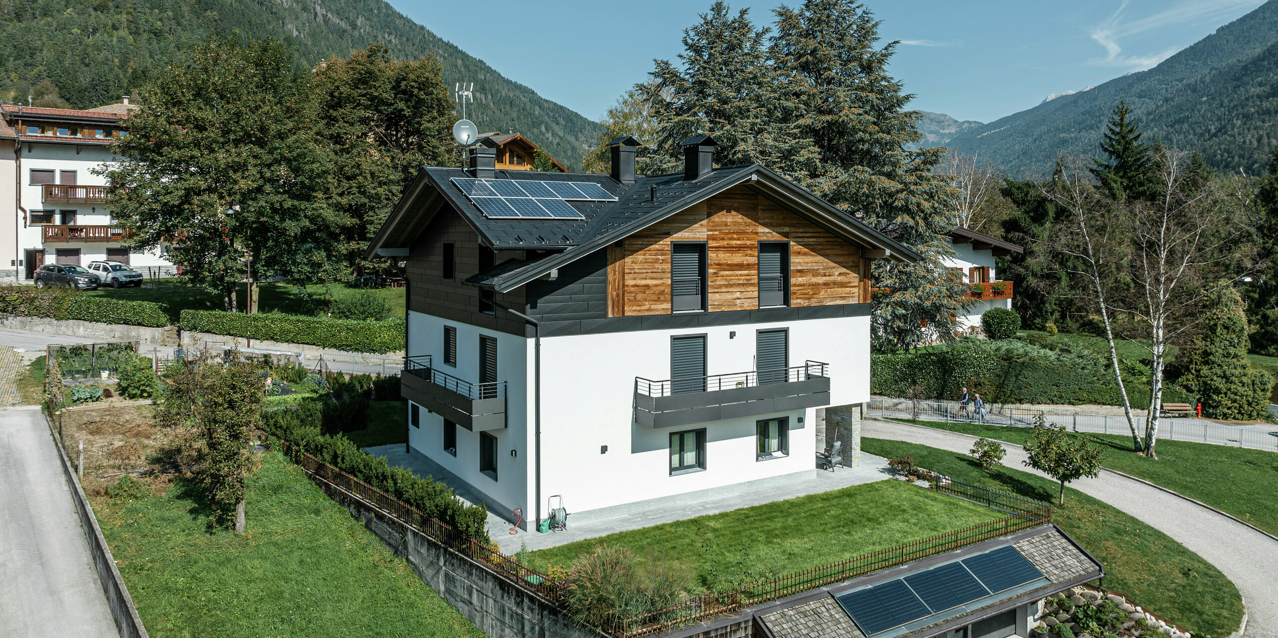 Bâtiment résidentiel modernisé à Pelugo, Italie, avec R.16 PREFA en P.10 anthracite et PREFA Siding.X sur la façade. La combinaison de l'aluminium, du bois et du plâtre garantit une architecture durable, résistante aux intempéries et élégante dans un environnement alpin. Des modules solaires sur le toit et le garage complètent le concept d'énergie durable.