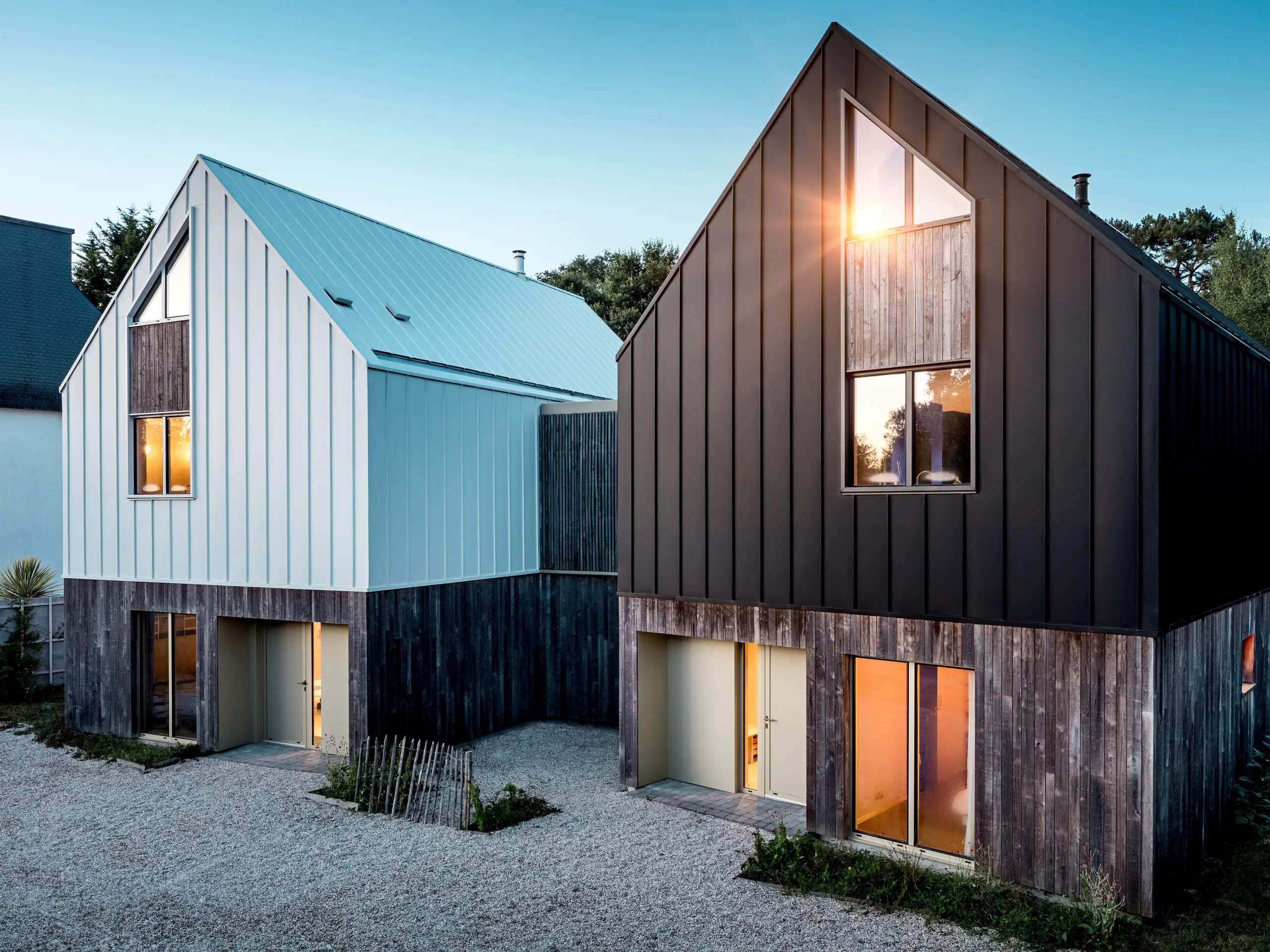 Les deux immeubles résidentiels du complexe Le Rhune se distinguent par leurs toitures à deux pans et leur bardage en aluminium PREFALZ, aux teintes contrastées de blanc pur P.10 et de gris-noir. Le design minimaliste, inspiré des maisons de pêcheurs bretonnes traditionnelles, est particulièrement réussi grâce à la précision des joints debout. La lumière intérieure chaleureuse crée des jeux de lumière captivants et met en valeur la présence architecturale des bâtiments à la structure épurée. L'enveloppe du bâtiment, durable et résistante aux intempéries, réalisée en PREFALZ, assure une liaison harmonieuse entre la toiture et la façade, permet des finitions soignées et confère au complexe une allure moderne, haut de gamme et intemporelle.