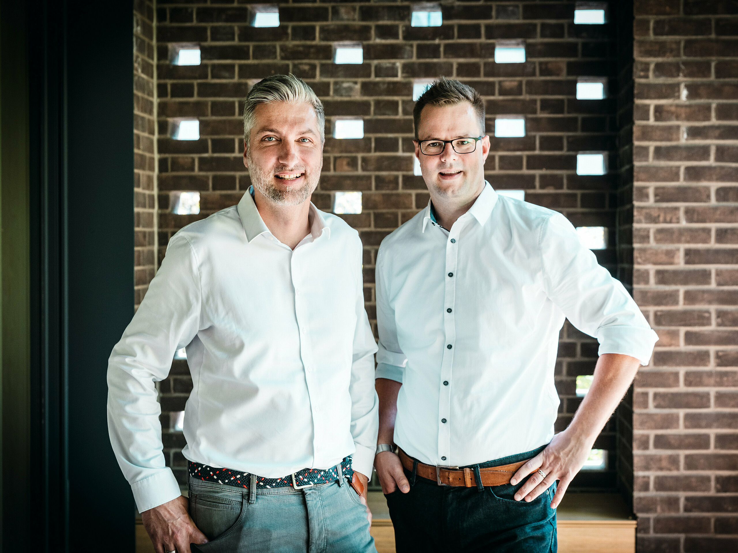 L'équipe d'architectes du cabinet A Fiúk Építész Stúdió se tient dans l'intérieur moderne d'une villa multigénérationnelle de Budapest, primée lors des PREFARENZEN 2026. Devant un mur de briques caractéristique, ils présentent la précision des matériaux et le langage stylistique de leur projet, notamment la toiture cubique en aluminium PREFALZ couleur P.10 anthracite. Cette scène met en lumière le savoir-faire architectural, la qualité d'exécution et le choix judicieux des matériaux, l'aluminium PREFA impressionnant par sa durabilité, la robustesse de son design et sa précision technique.