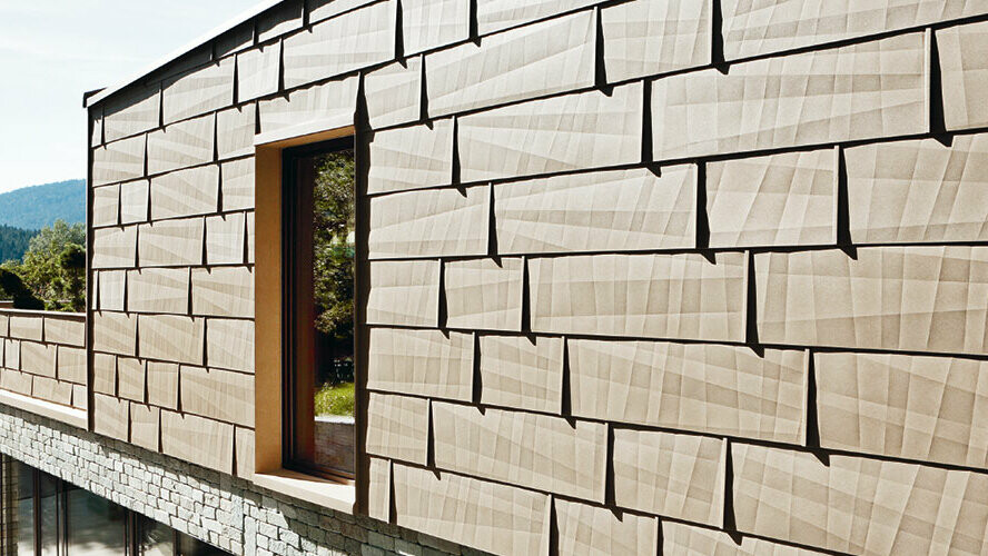 Sur cette façade extérieure, le panneau de façade FX.12 PREFA couleur P.10 brun sable est associé à une façade en pierre au rez-de-chaussée.