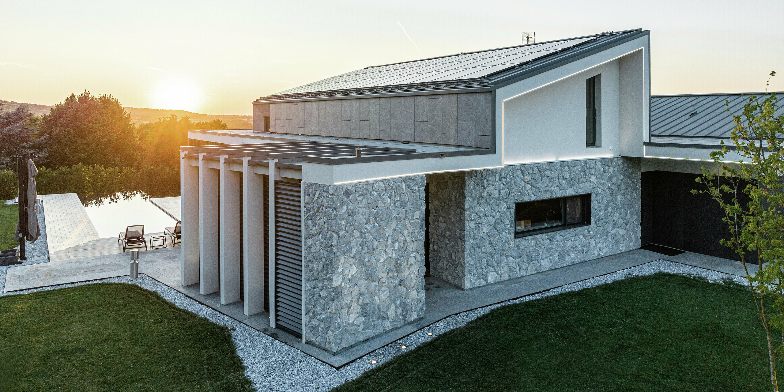 Vue détaillée de la luxueuse maison individuelle à Scandiano, Italie. Les toitures PREFALZ en P.10 anthracite assurent une apparence moderne et élégante et offrent une protection optimale contre les intempéries. La façade en pierre naturelle et les lignes claires du design s'harmonisent parfaitement avec la solution de toiture PREFA de haute qualité et l'architecture bien pensée.