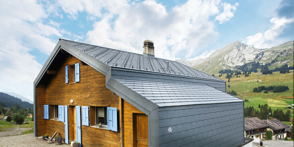 Maison dans les montagnes suisses avec façade en bois, combinée au losange de toiture et de façade PREFA couleur gris pierre
