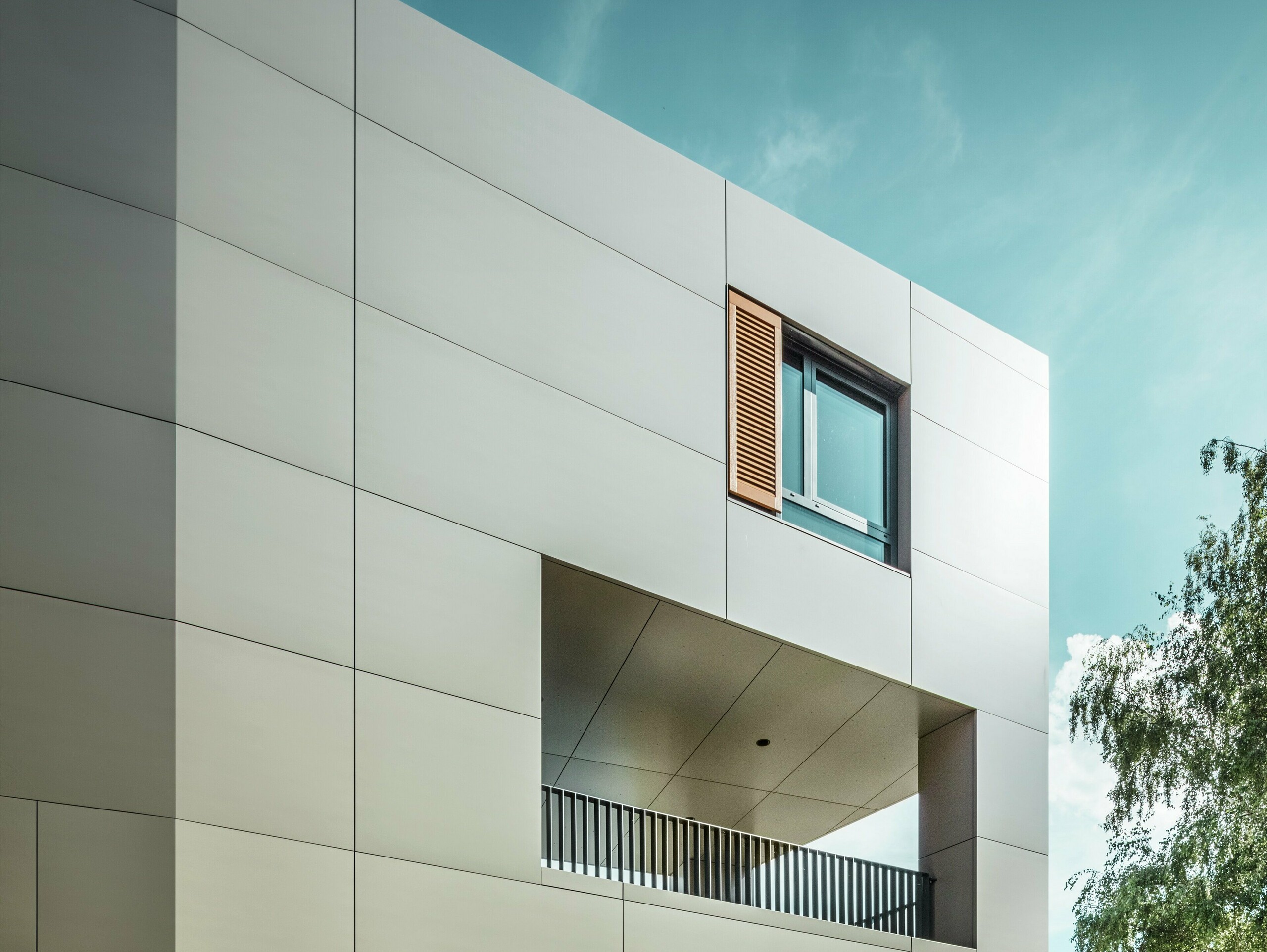 La photo montre la mairie moderne d'Alzenau avec une façade en panneaux composites en aluminium PREFA couleur bronze. L'architecture se caractérise par des formes géométriques claires et de grandes fenêtres. La toiture pointue et l'éclairage discret confèrent au bâtiment un aspect élégant et contemporain.