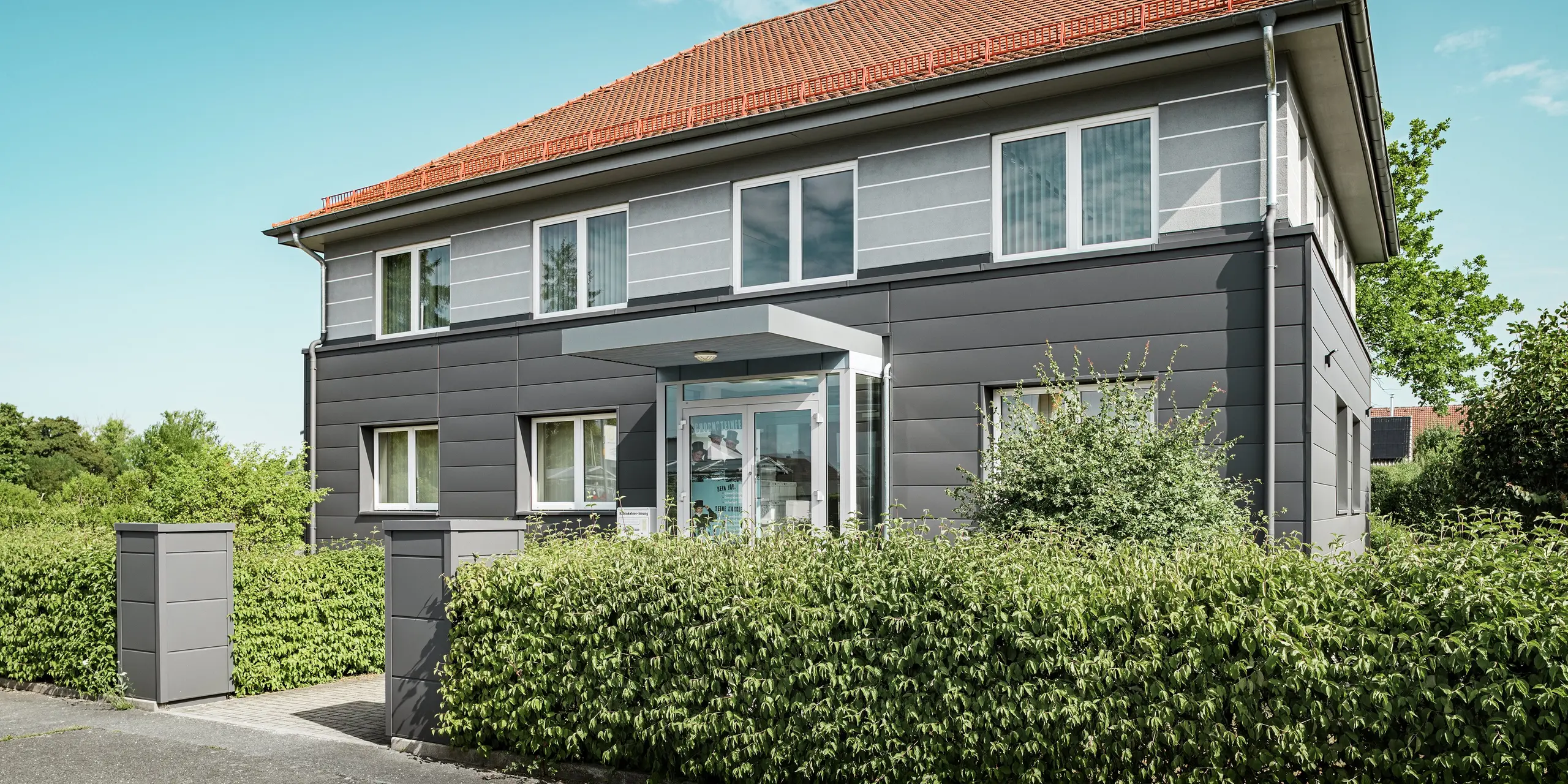 La façade modernisée de la guilde des ramoneurs de Bindlach est revêtue de panneaux PREFA P.10 gris sombre. Ces panneaux en aluminium confèrent au bâtiment rénové une allure élégante et contemporaine. Posés avec précision et s'étendant jusqu'à l'entrée, ils protègent efficacement la structure et garantissent une conception de façade durable. Ce matériau est facile d'entretien, résistant et s'intègre harmonieusement à son environnement naturel.