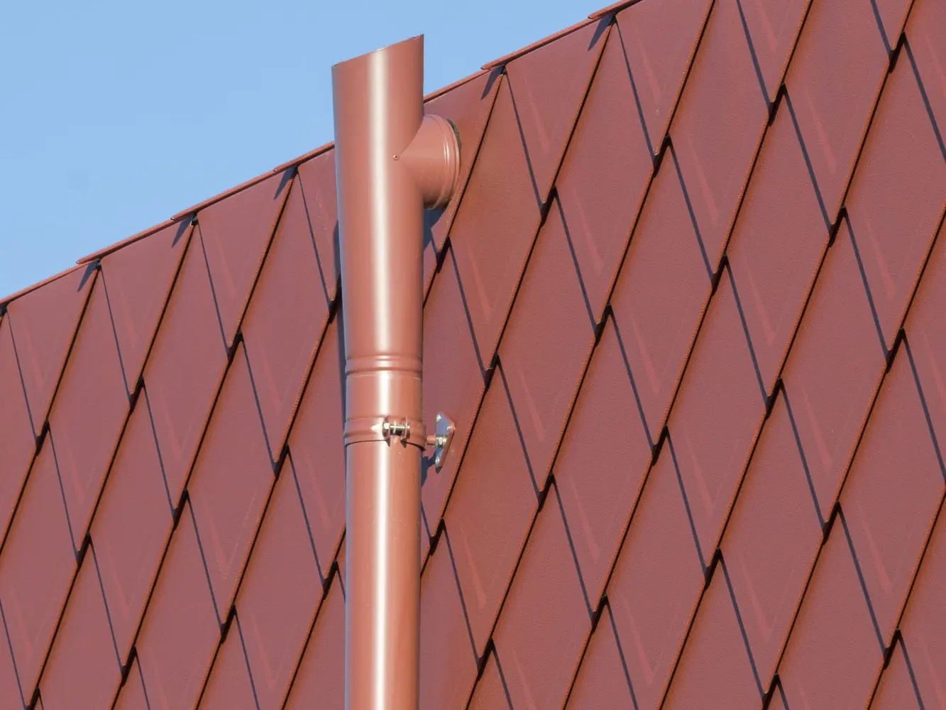 Zoom sur les évacuations des eaux, système complet PREFA, dans la même teinte P.10 rouge oxyde que les losanges de façade