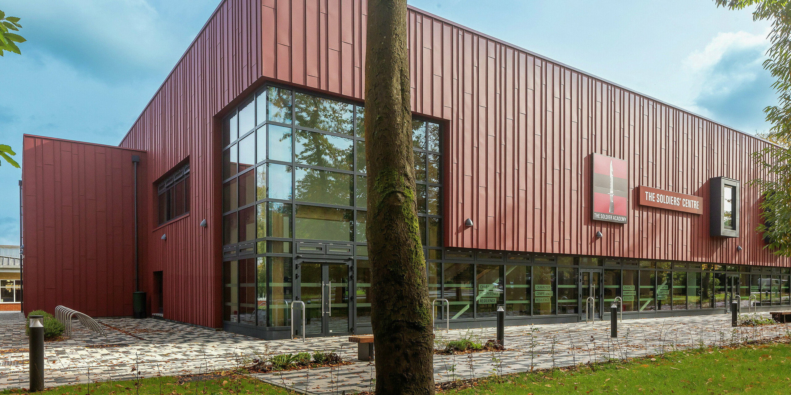Conception de façade innovante avec PREFALZ : le Soldiers' Centre de Pirbright impressionne par son revêtement moderne à joint debout en PREFALZ en P.10 rouge oxyde. Les surfaces vitrées généreuses créent une atmosphère lumineuse et accueillante, tandis que les cadres de fenêtres en P.10 anthracite ajoutent des accents élégants. Durabilité, résistance et design combinés - des produits en aluminium PREFA de haute qualité pour une architecture tournée vers l'avenir.