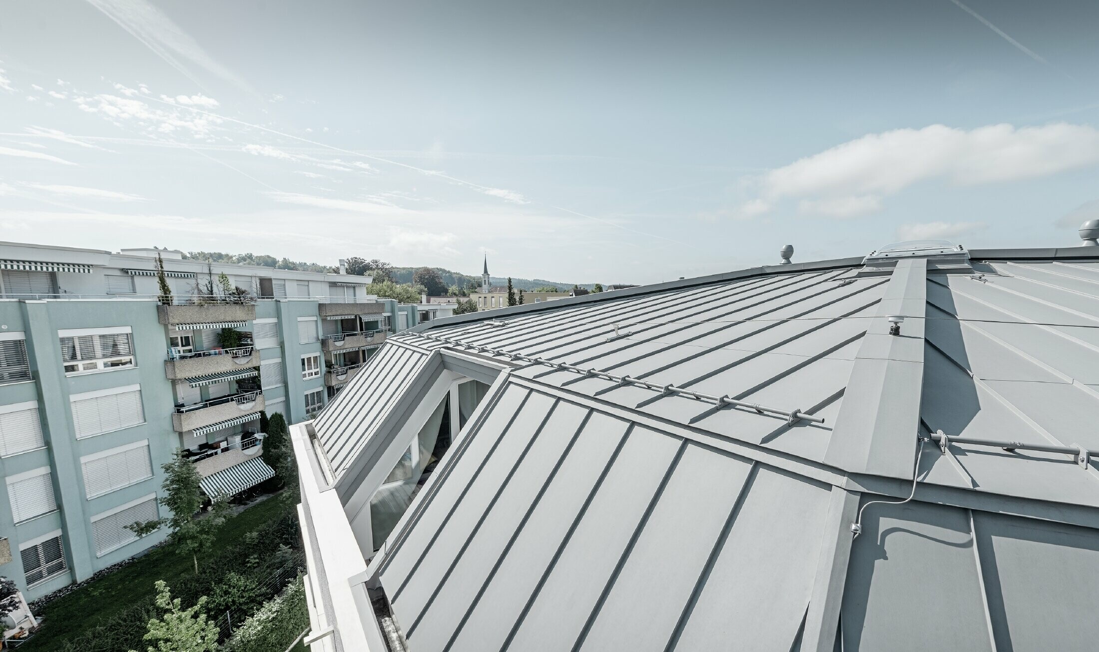 Vue détaillée de la surface de toiture d’un immeuble collectif ; toit à joint debout réalisé avec Prefalz PREFA couleur gris quartz.