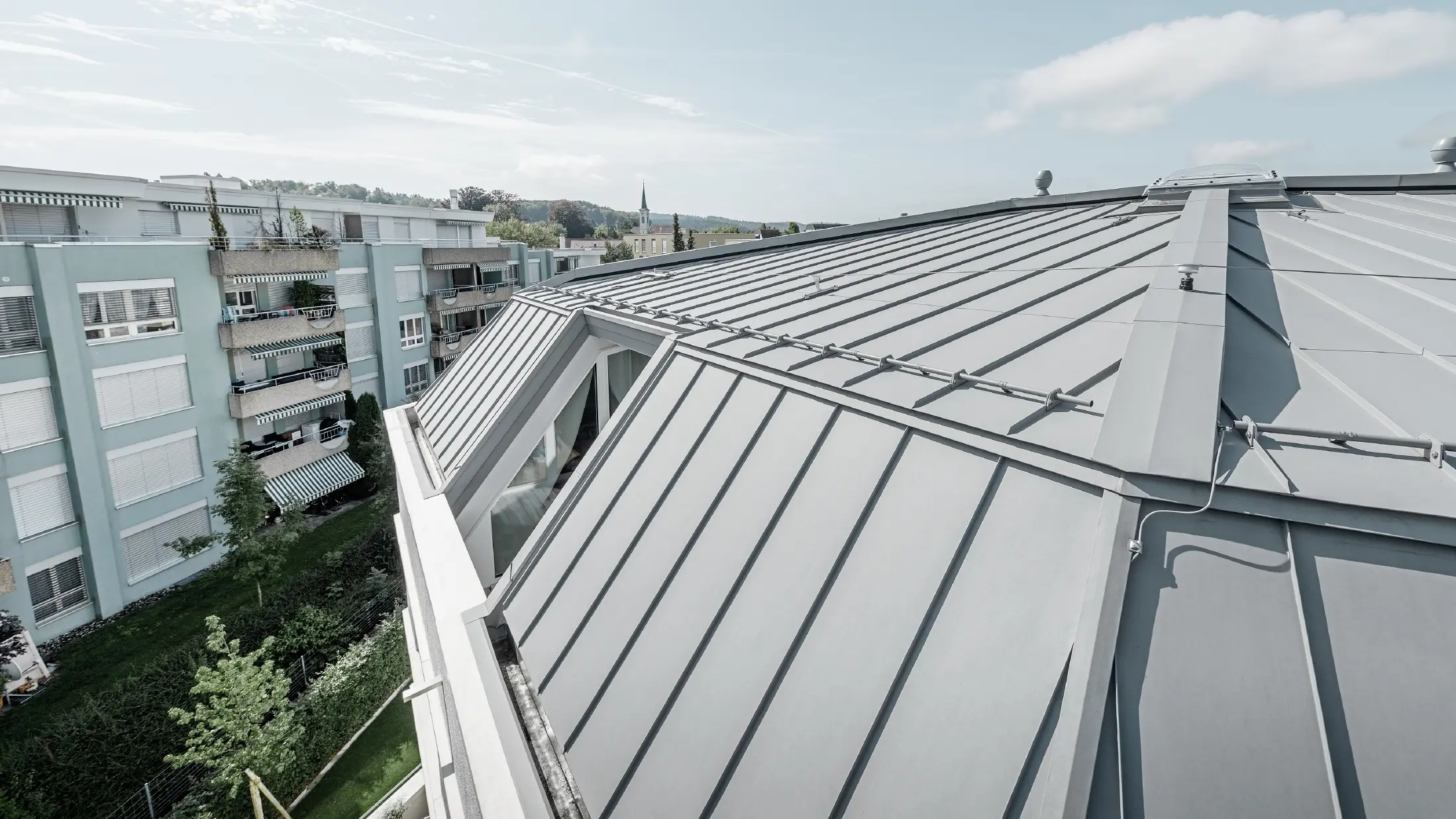 Vue détaillée de la surface de toiture d’un immeuble collectif ; toit à joint debout réalisé avec Prefalz PREFA couleur gris quartz.