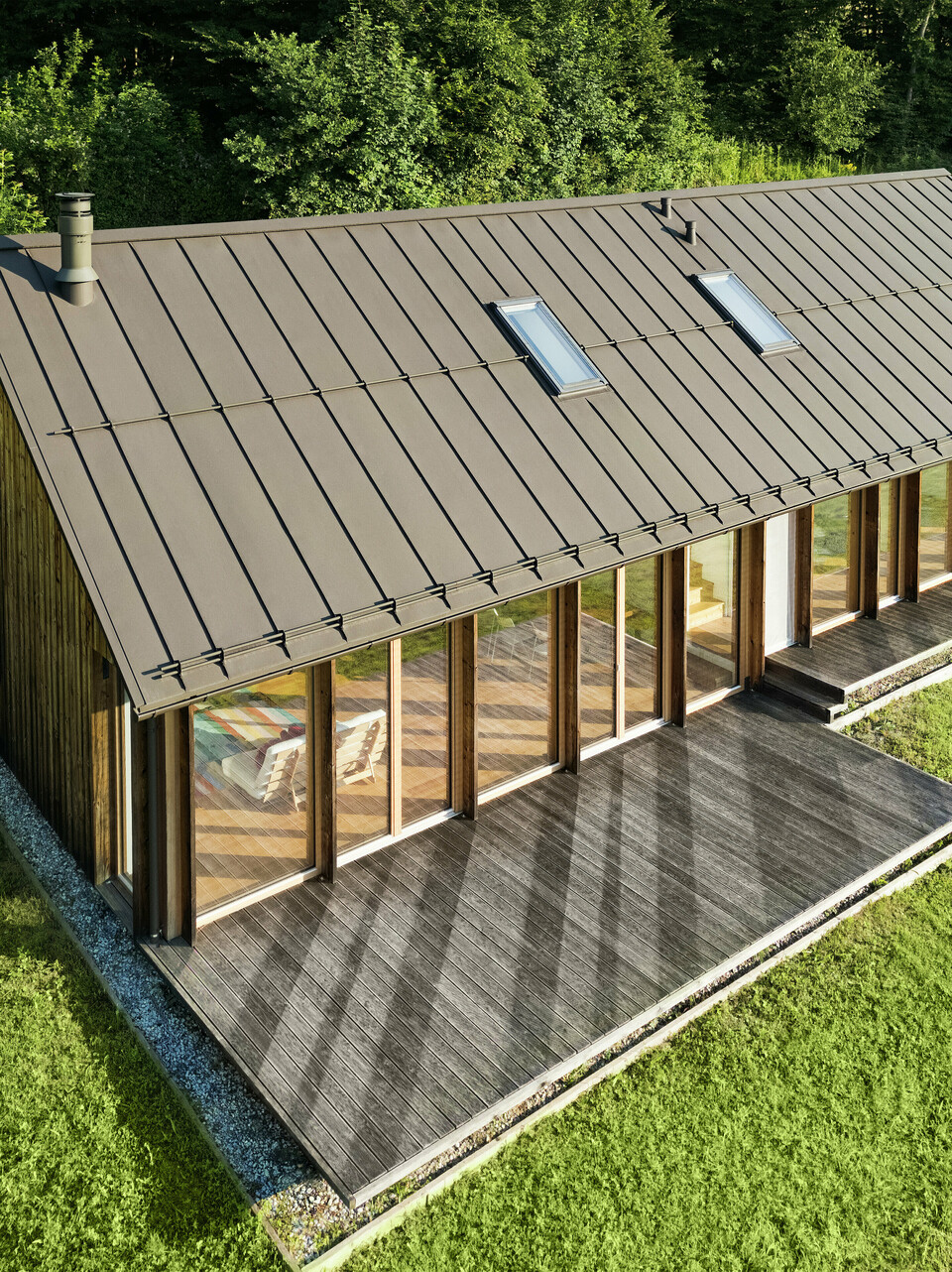 Maison en bois moderne avec une grande façade vitrée et un toit en aluminium PREFALZ résistant de couleur P.10 brun – idéale pour les terrains en pente comme à Vinje. La couverture de toit de haute qualité offre une résistance maximale aux intempéries, une longue durée de vie et une esthétique élégante. Grâce à la pose précise des joints debout et à l’intégration de fenêtres de toit, un concept d’habitat durable et baigné de lumière voit le jour. La vue en plongée met en évidence la finition soignée des joints debout en aluminium.