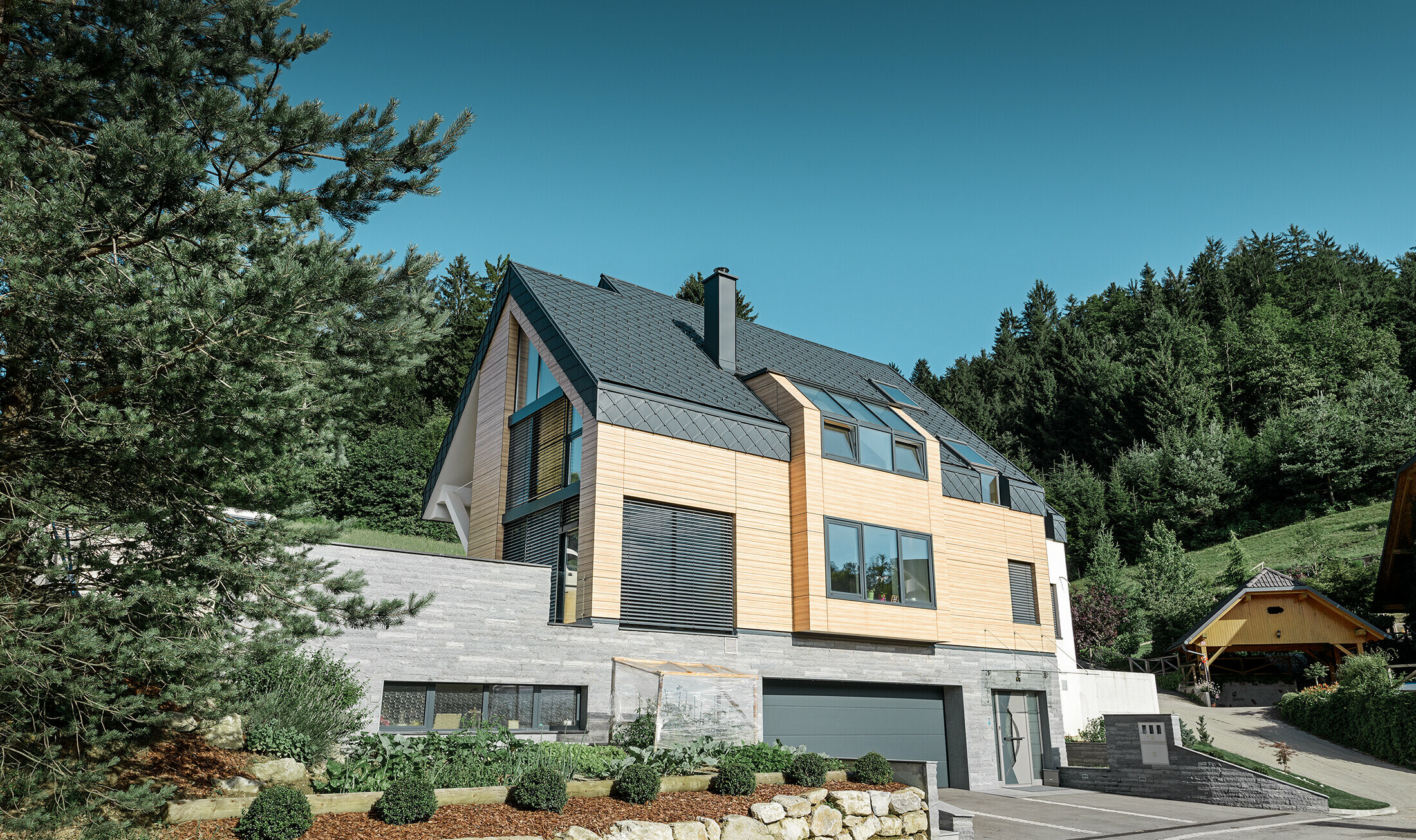 Maison individuelle au toit à deux versants sans saillie de toit — Façade à l’aspect du bois et toiture en aluminium PREFA de couleur anthracite