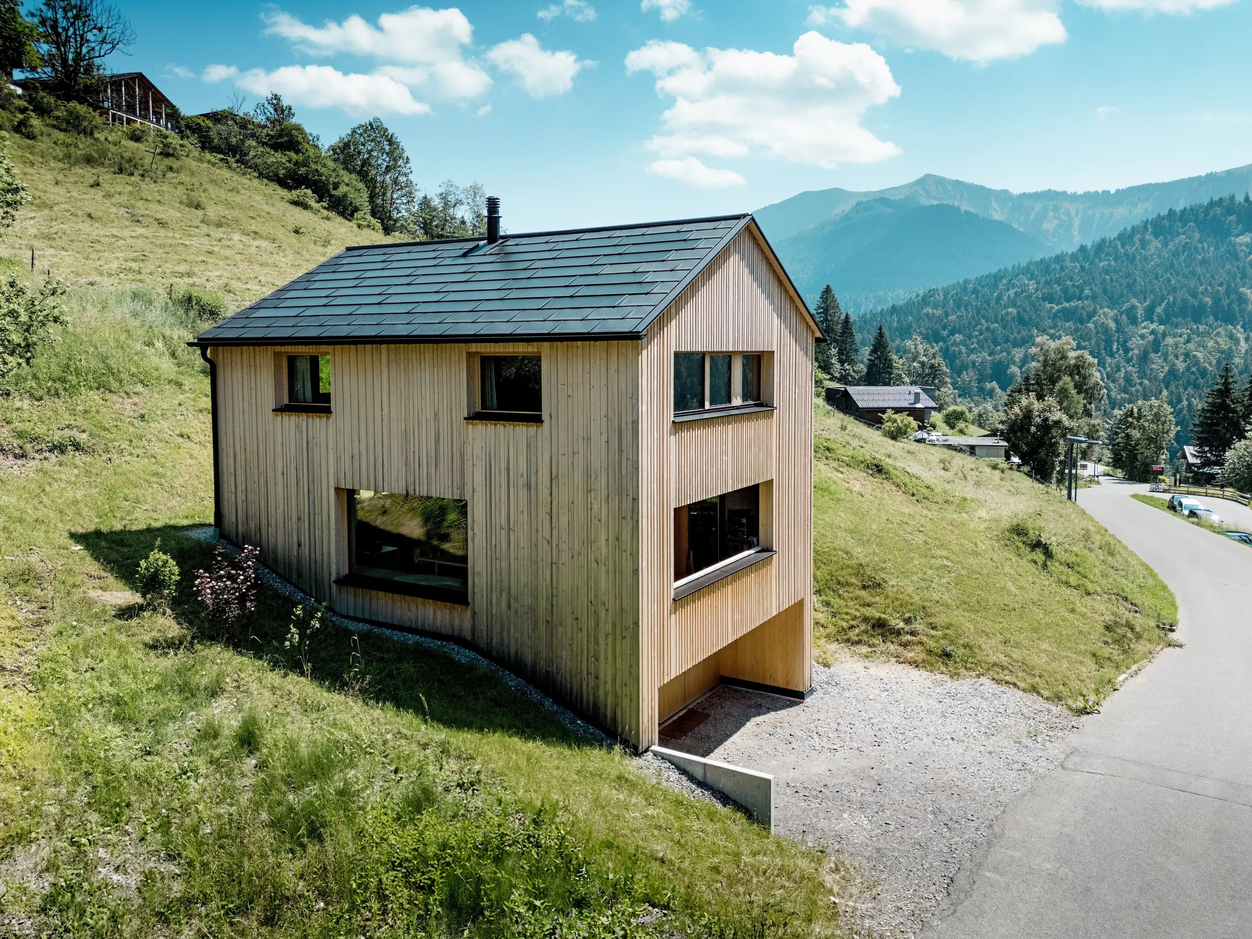 Perchée au-dessus de la vallée, la maison Immi se dresse telle un monolithe de bois épuré sur le versant ensoleillé d’Ebnit. La façade sobre en sapin blanc et le toit solaire PREFA noir créent un contraste saisissant avec l’immensité du paysage alpin. Les tuiles solaires intégrées et les R.16 en P.10 Noir produisent de l’énergie solaire, résistent aux conditions météorologiques alpines et garantissent une toiture durable et harmonieuse.