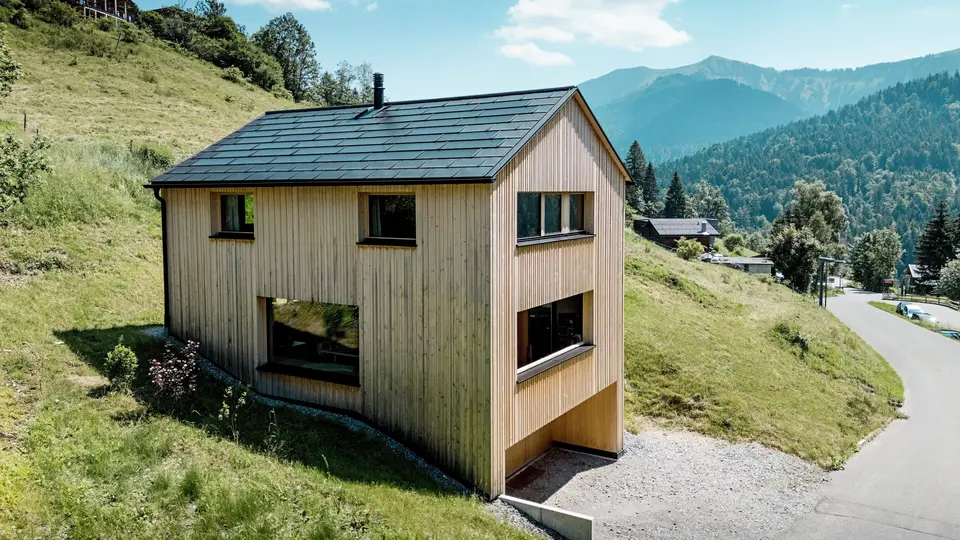 Perchée au-dessus de la vallée, la maison Immi se dresse telle un monolithe de bois épuré sur le versant ensoleillé d’Ebnit. La façade sobre en sapin blanc et le toit solaire PREFA noir créent un contraste saisissant avec l’immensité du paysage alpin. Les tuiles solaires intégrées et les R.16 en P.10 Noir produisent de l’énergie solaire, résistent aux conditions météorologiques alpines et garantissent une toiture durable et harmonieuse.
