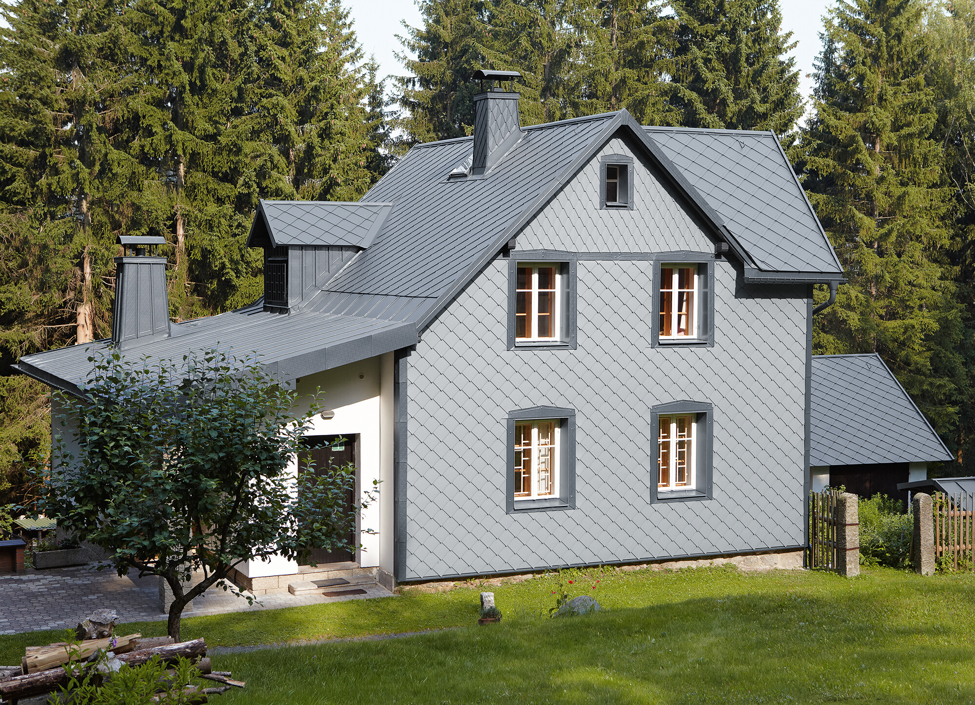 Façade avec losange de façade PREFA 29 × 29 en gris souris sur le côté exposé aux intempéries Maison individuelle dans un espace boisé avec façade en aluminium PREFA résistante aux intempéries en gris souris.