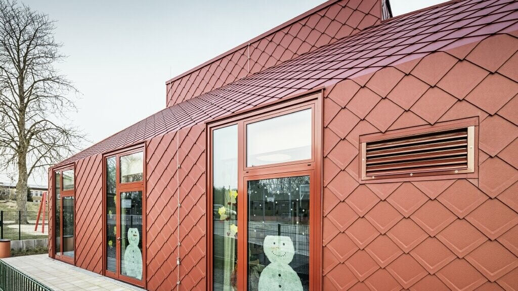 Vue de face de la crèche Le bonhomme de neige collé aux fenêtres en rappelle la saison. La crèche de Hennstedt est recouverte avec le losange de toiture 29 × 29 en rouge oxyde.