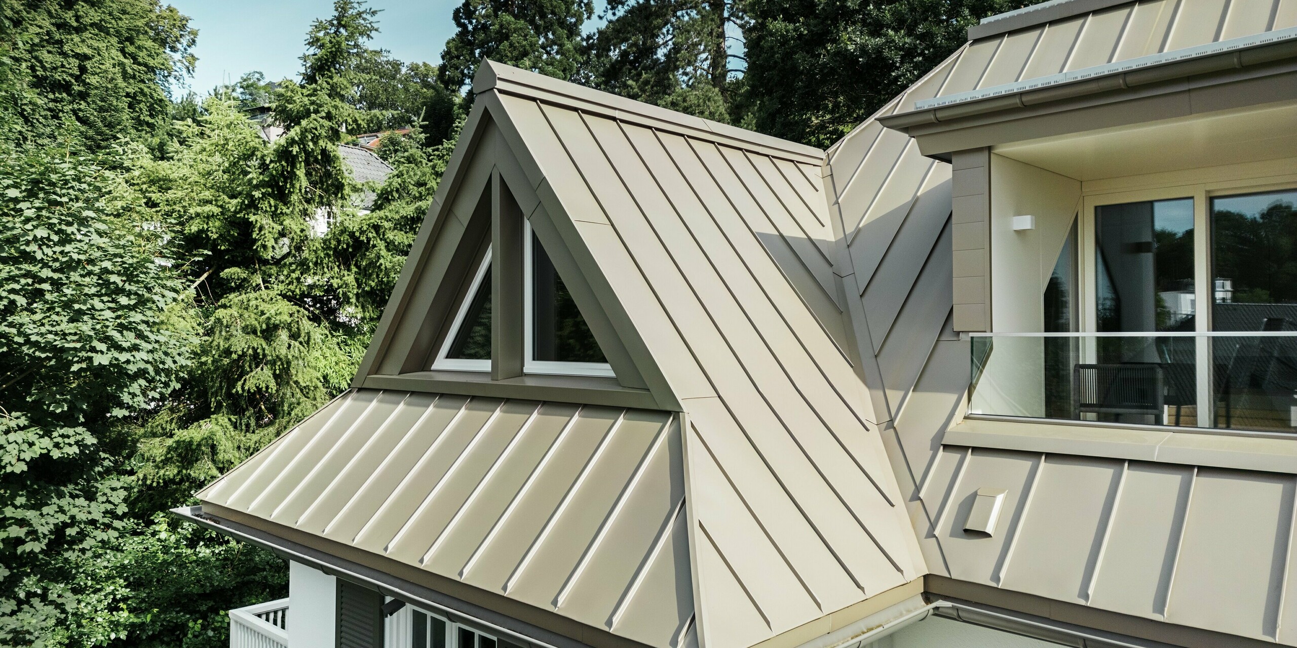 Cette vue met en valeur les fenêtres de toit de la Villa Blankenese et leurs lucarnes remarquables, revêtues de PREFALZ couleur bronze. Un élégant balcon est visible sur la droite. Le revêtement en aluminium à joints debout, d'une grande précision, souligne l'architecture épurée du bâtiment et assure une protection durable contre les intempéries. La surface bronze reflète magnifiquement la lumière, conférant à la villa une allure moderne et haut de gamme. Les produits en aluminium PREFALZ sont résistants à la corrosion, légers et sans entretien – idéaux pour les toitures et façades durables des projets de construction les plus exigeants.